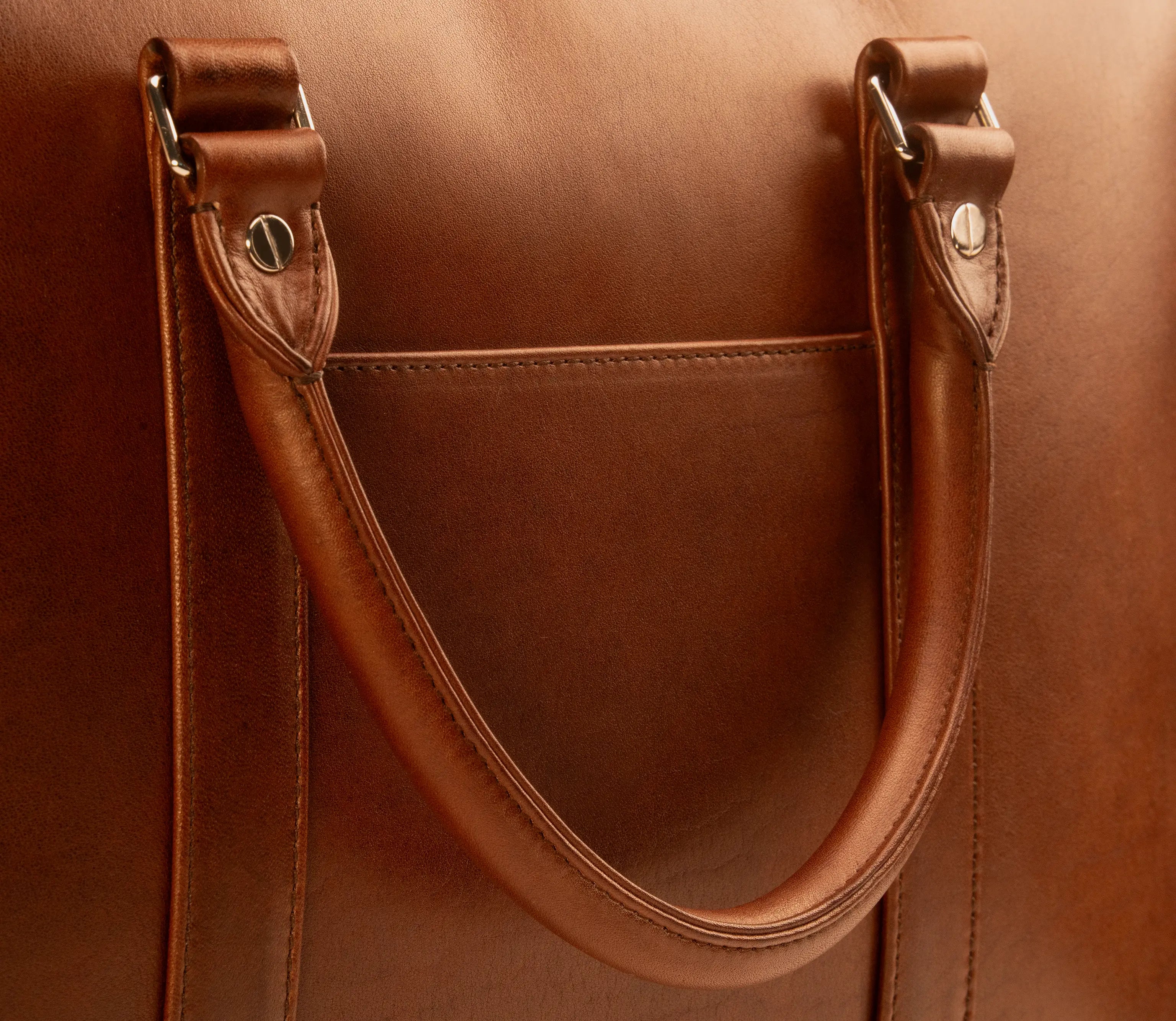 Detail of the Lunburg Opus Briefcase in Deep Mahogany showing the folded leather handle loop, L-branded 316L stainless steel studs, slip pocket, and saddle stitching in vegetable-tanned Perpetual Leather (from Tempesti).