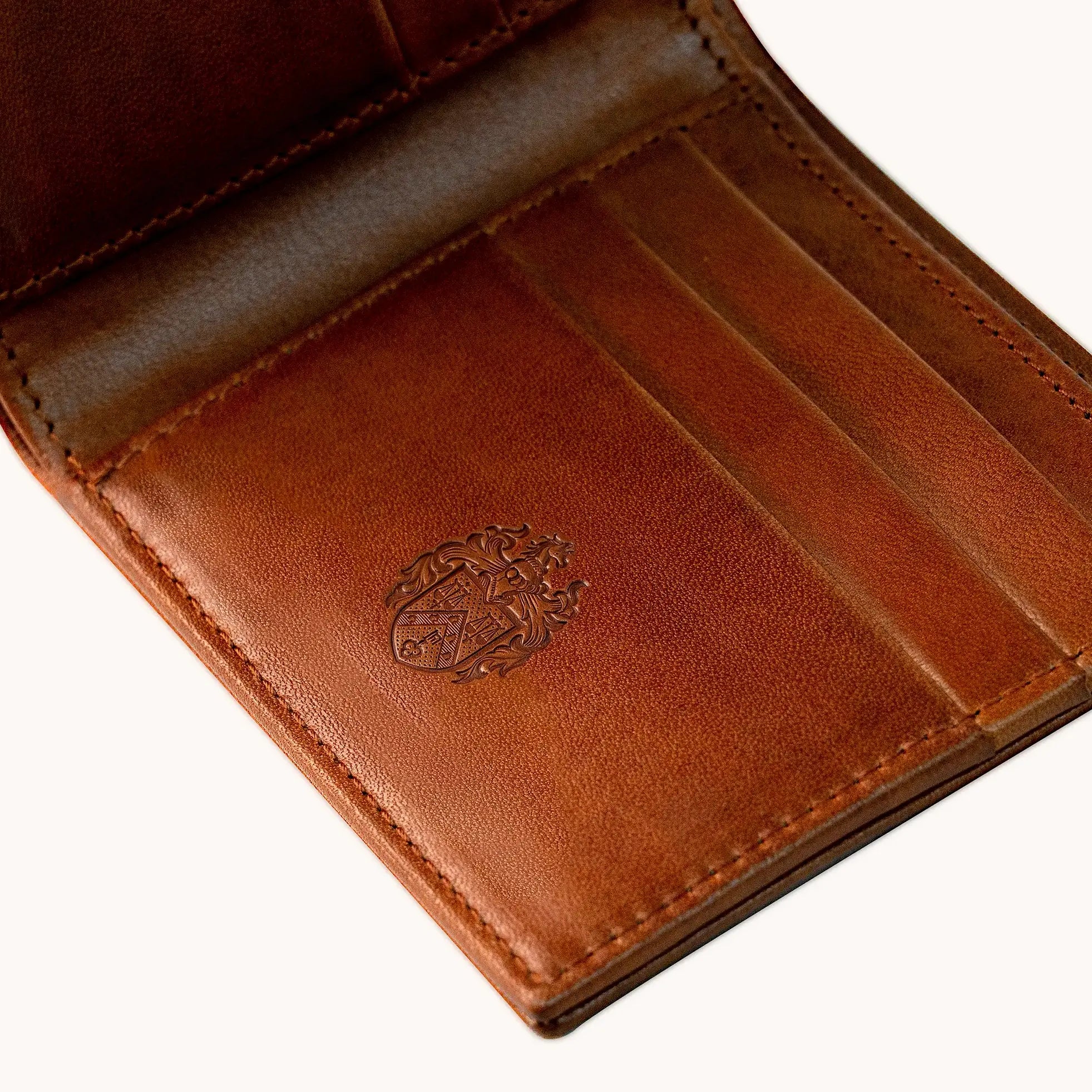 Interior of a Lunburg Horizontal Signet wallet in Heritage Amber showing a heat-embossed family crest on the card slot panel, the Inscription service that transforms a commission into an heirloom, in vegetable-tanned Perpetual Leather with folded edge construction.