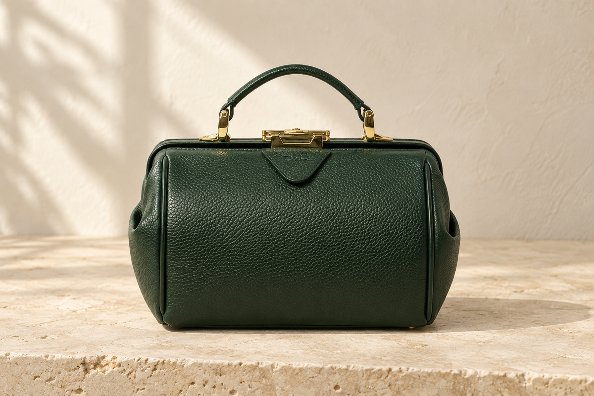 Illustrative rectangular handbag with rounded corners, a raised perimeter seam, central clasp and one short arched handle.