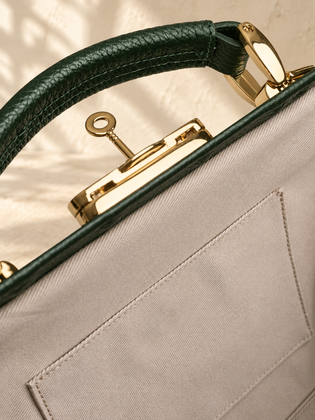 Detail of the illustrative handbag showing a key in the clasp, narrow rim, stitched pocket edge and short-handle mount.