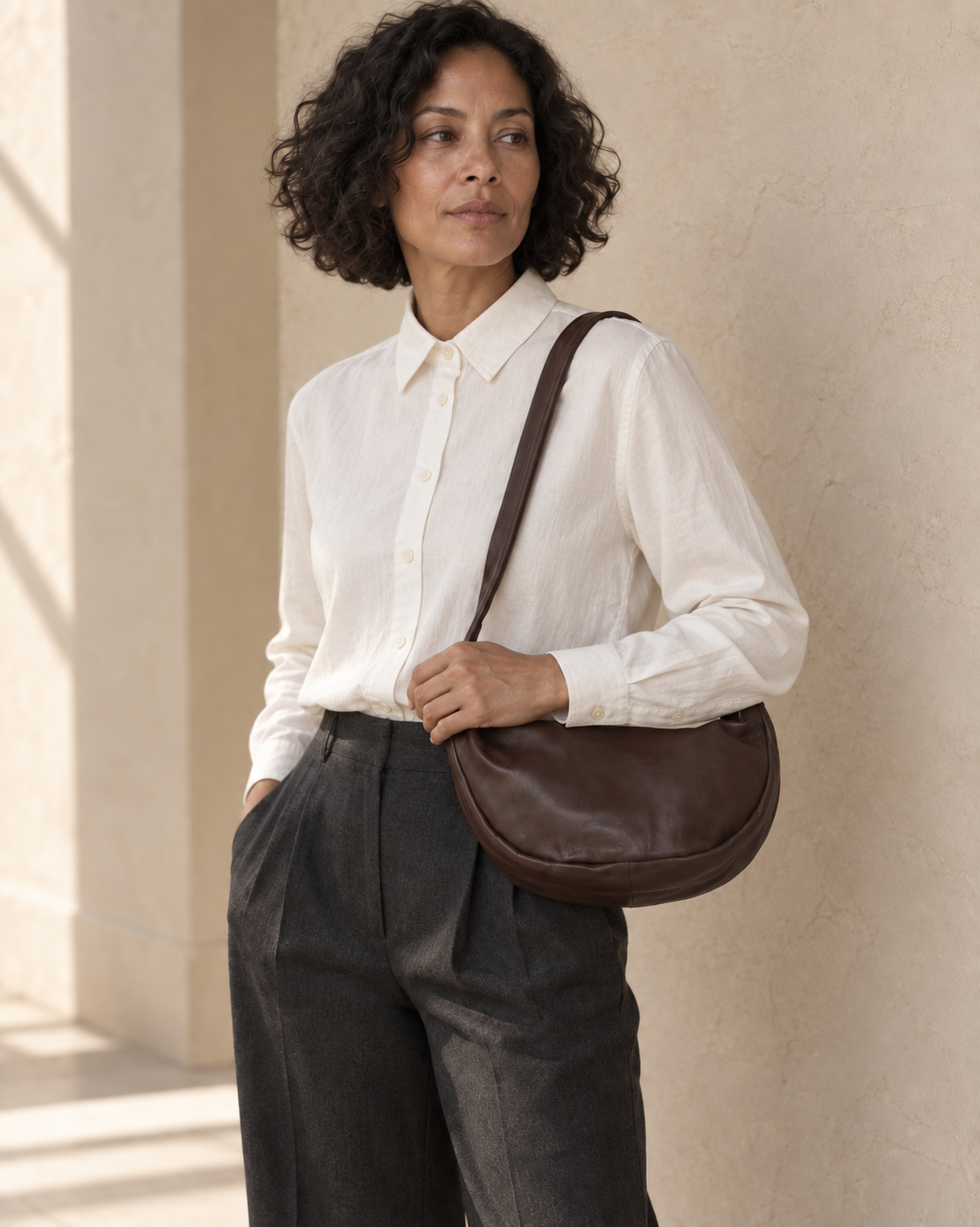 Model view of the illustrative crescent bag showing the curved silhouette and wide flexible shoulder strap.