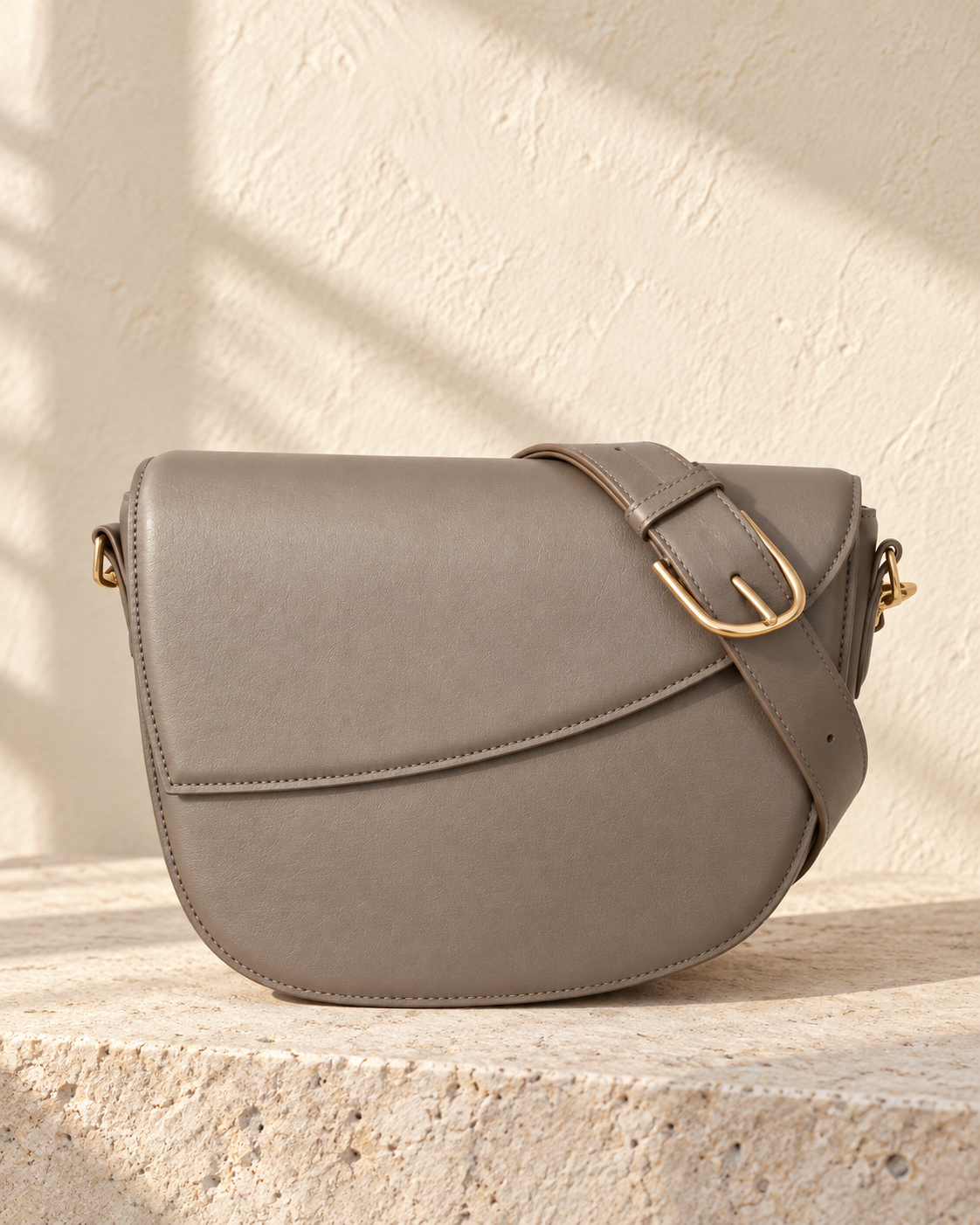 Illustrative rounded crossbody with an asymmetric curved flap and visible stitching around its perimeter.
