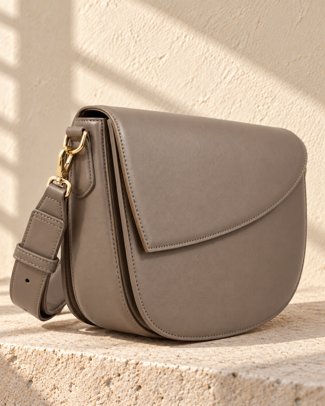 Three-quarter view of the illustrative curved-flap crossbody showing a side gusset and adjustable strap clipped to side rings.