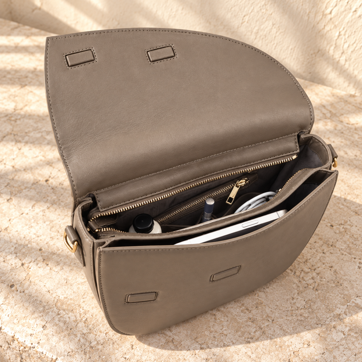 Open view of the illustrative crossbody showing covered rectangular closure pads, a zipped inner opening and slip section.