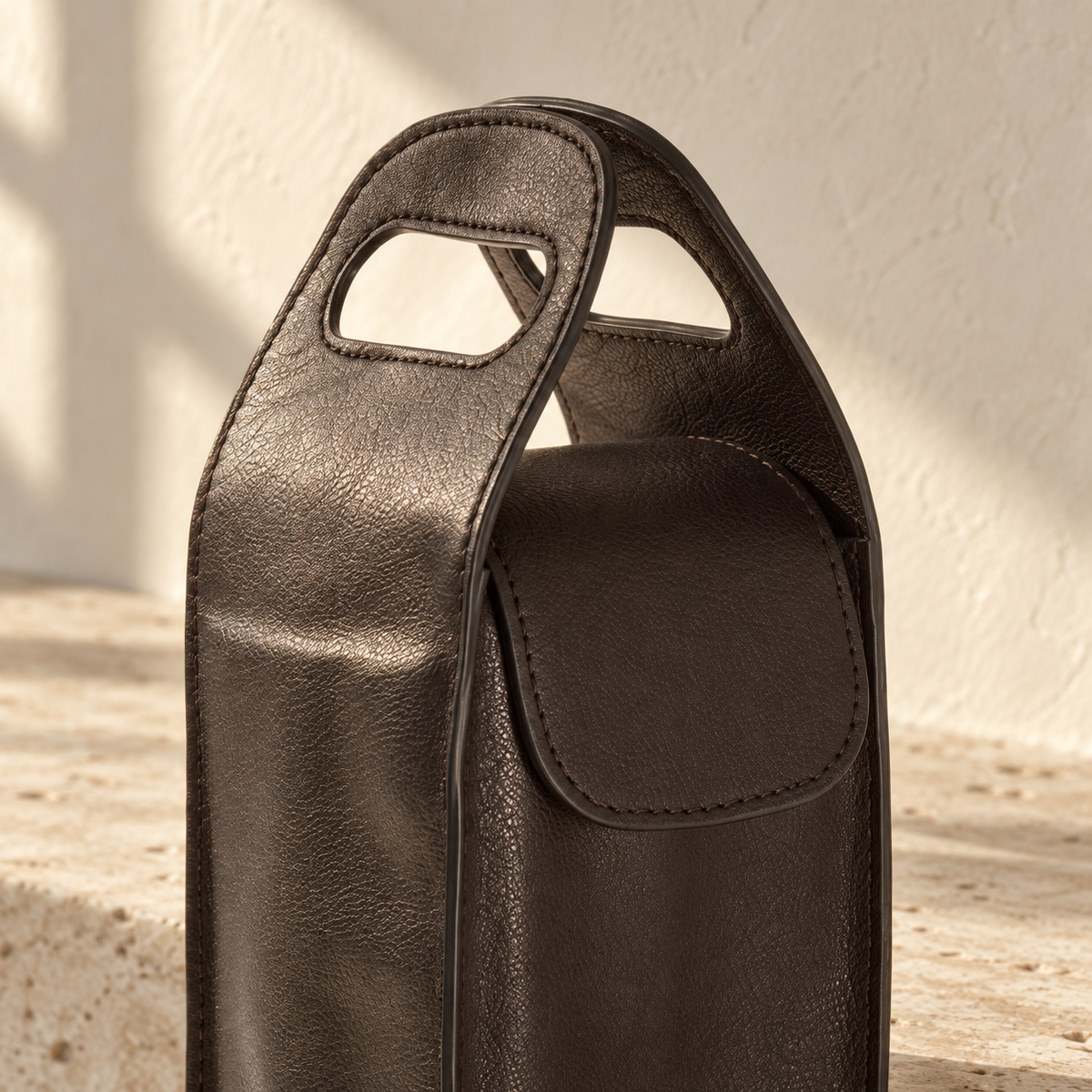 Illustrative cutout-handle bottle carrier, view 3: close view shows paired handle cutouts, curved flap and visible edge stitching.