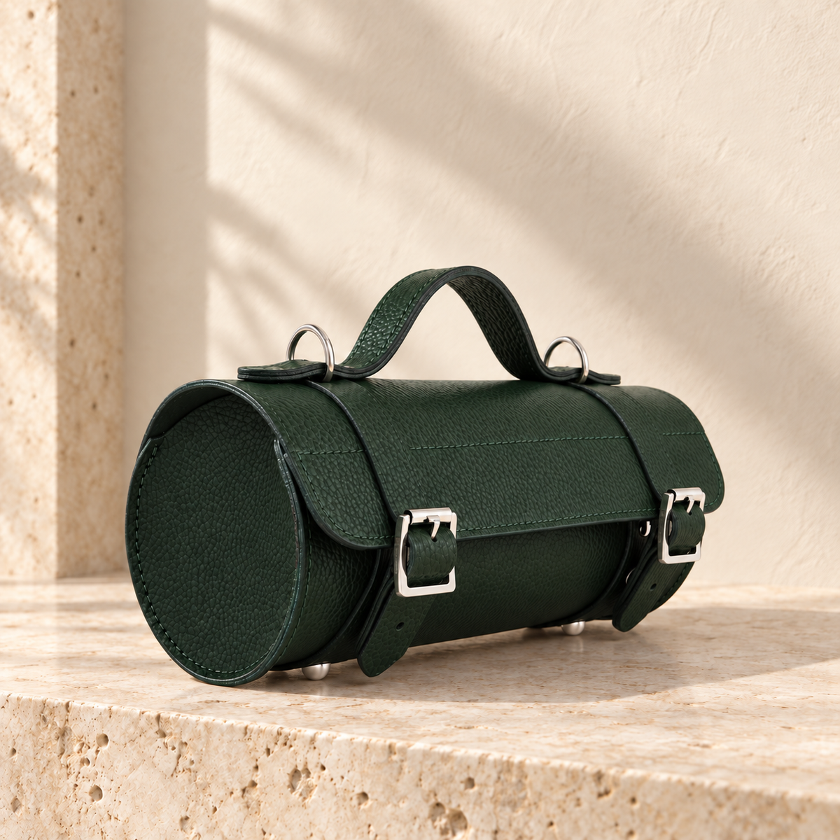Illustrative cylindrical handbag with circular stitched ends, an overlapping flap, two buckle-look straps and a bridge handle.
