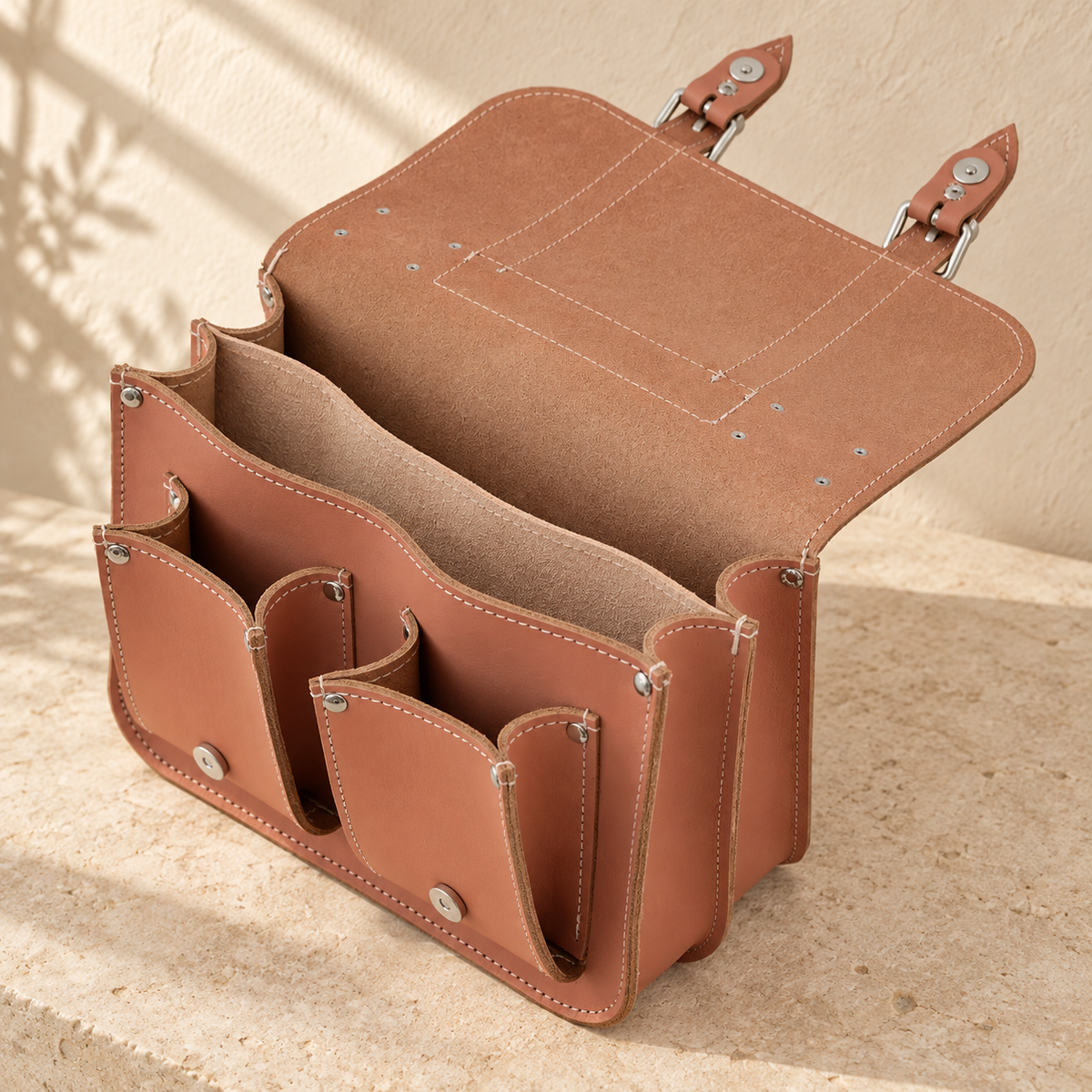 Open illustrative satchel showing a full-width divider, two main internal spaces and release discs beneath the raised buckled flap.