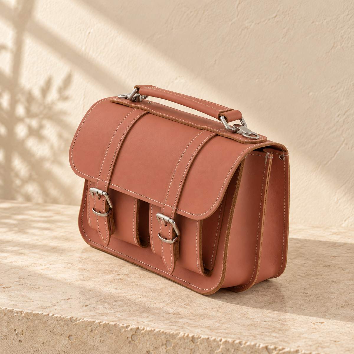Detail of the illustrative satchel showing divided side gussets, exposed brown edges and the handle’s metal fittings.