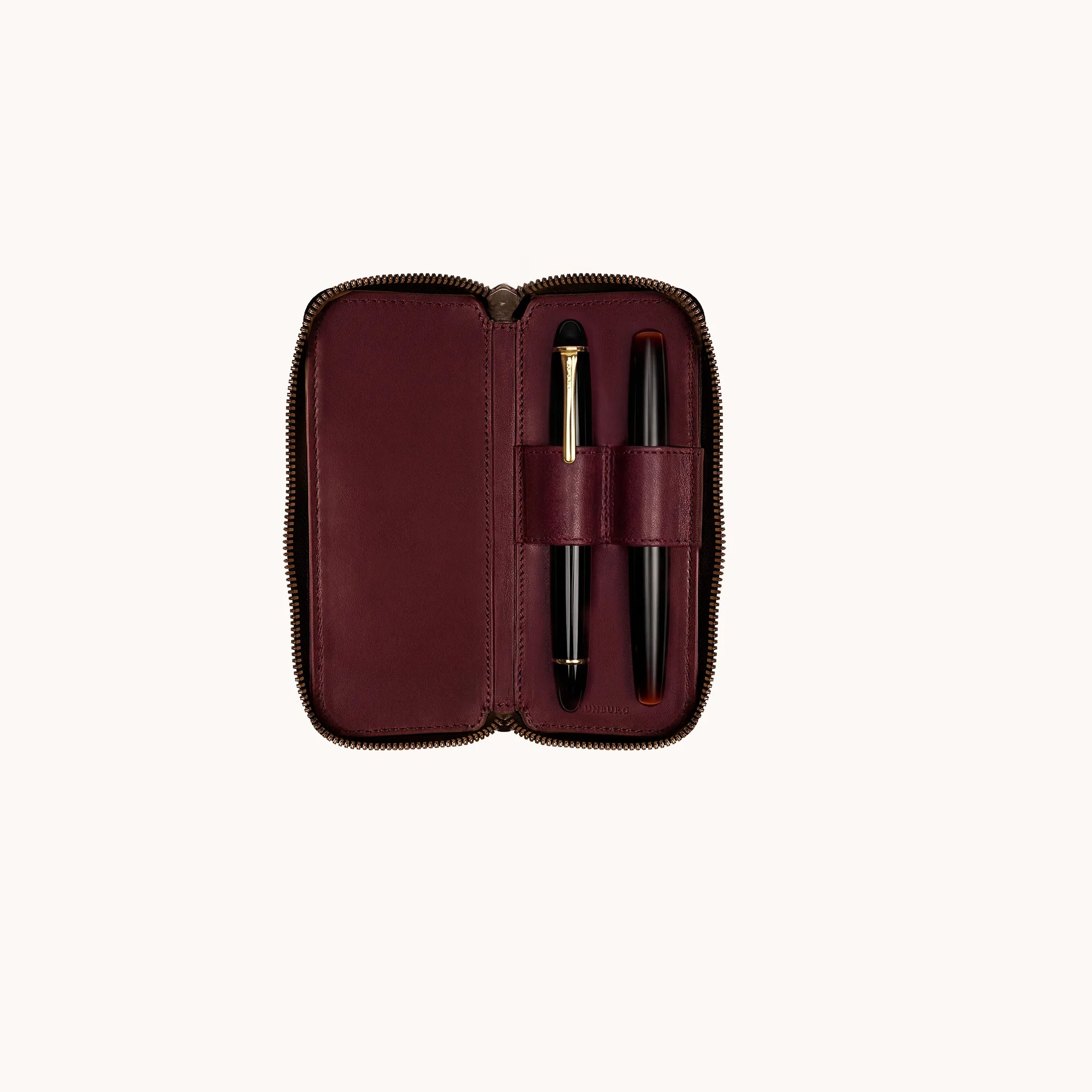 Lunburg Double Pen Case Curator in Deep Mahogany, interior view with Montblanc Meisterstück and Nakaya fountain pen seated in the two leather pen loops, goat leather lining shown across the full interior, heat-embossed Lunburg mark at lower edge, YKK Excella zipper framing the perimeter.
