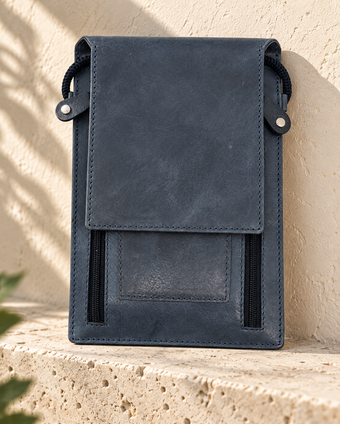 Illustrative upright travel document pouch with a full flap, perimeter stitching, side cords and two exposed zip tracks.
