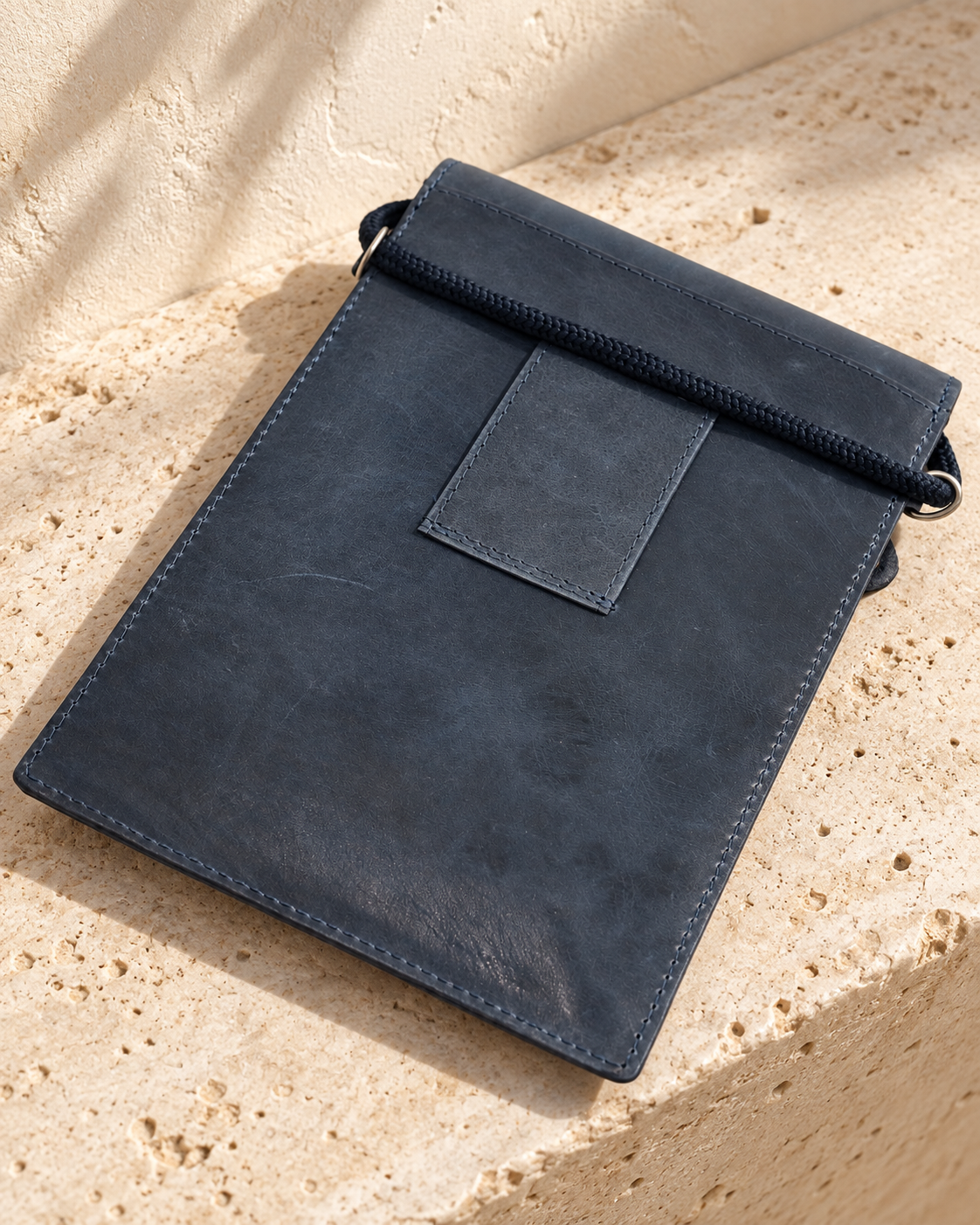 Rear of the illustrative travel document pouch showing a broad belt-loop strip and cord passing across the top.