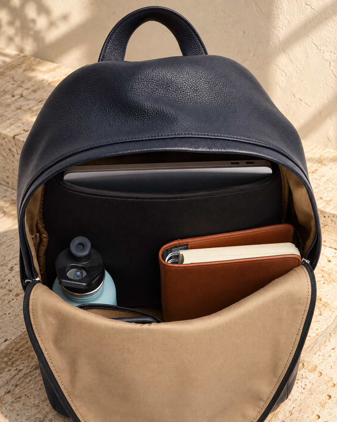 Interior of the illustrative daypack showing tan textile-look lining and a broad dark rear sleeve with objects inside.