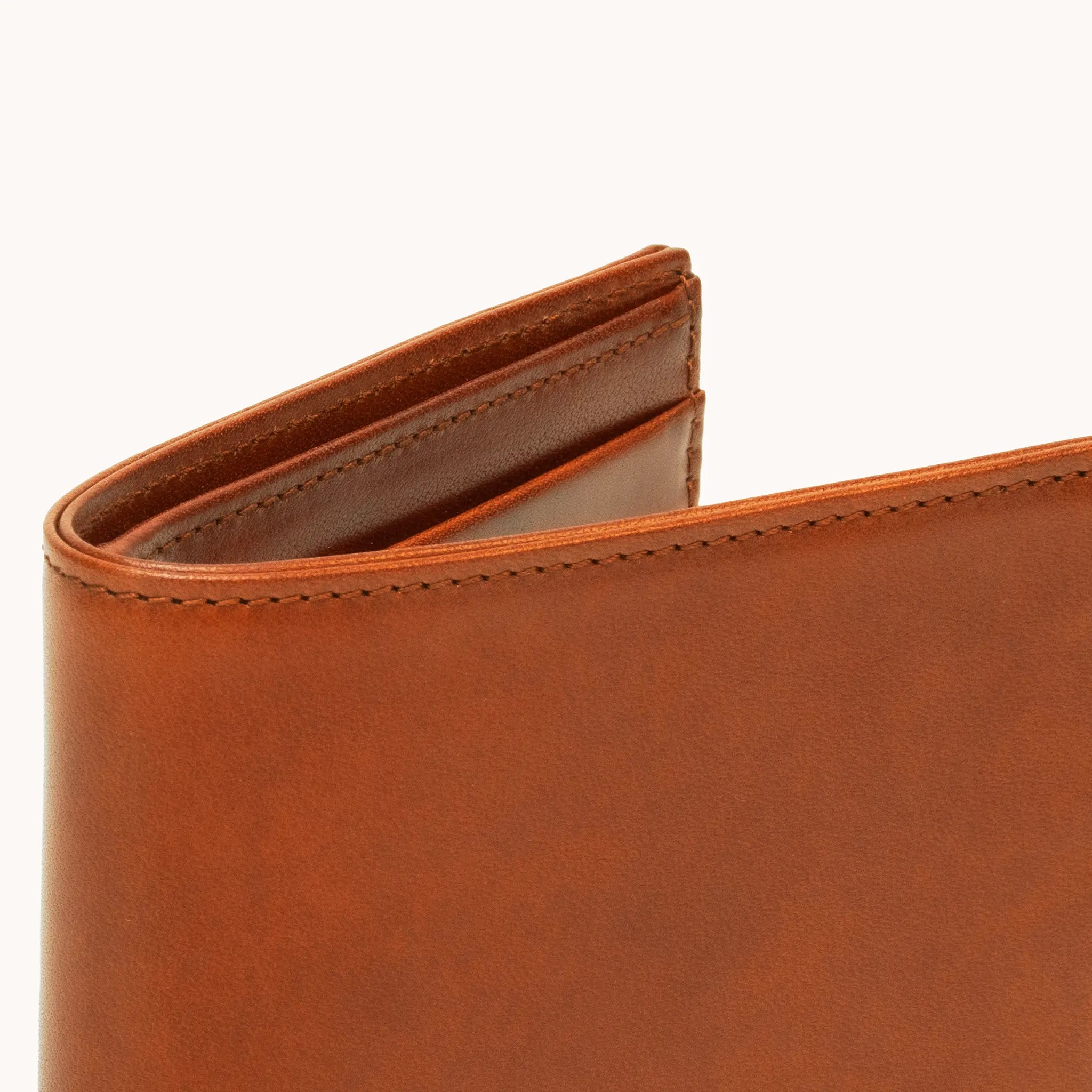 Close-up of the upper spine and fold of the Lunburg Horizontal Signet Bifold Wallet in Heritage Amber, showing folded edge construction, edge stitching, and interior glimpse in vegetable-tanned Perpetual Leather.