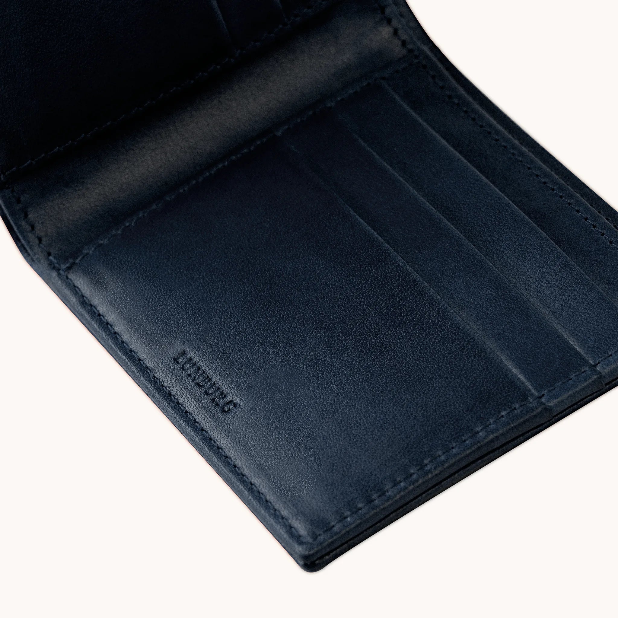 Lunburg Signet Horizontal Bifold in Nocturnal Sapphire, angled interior detail showing the card slot layering, heat-embossed Lunburg mark, and goat leather lining with folded edge construction throughout, in vegetable-tanned Perpetual Leather (from Tempesti)."
