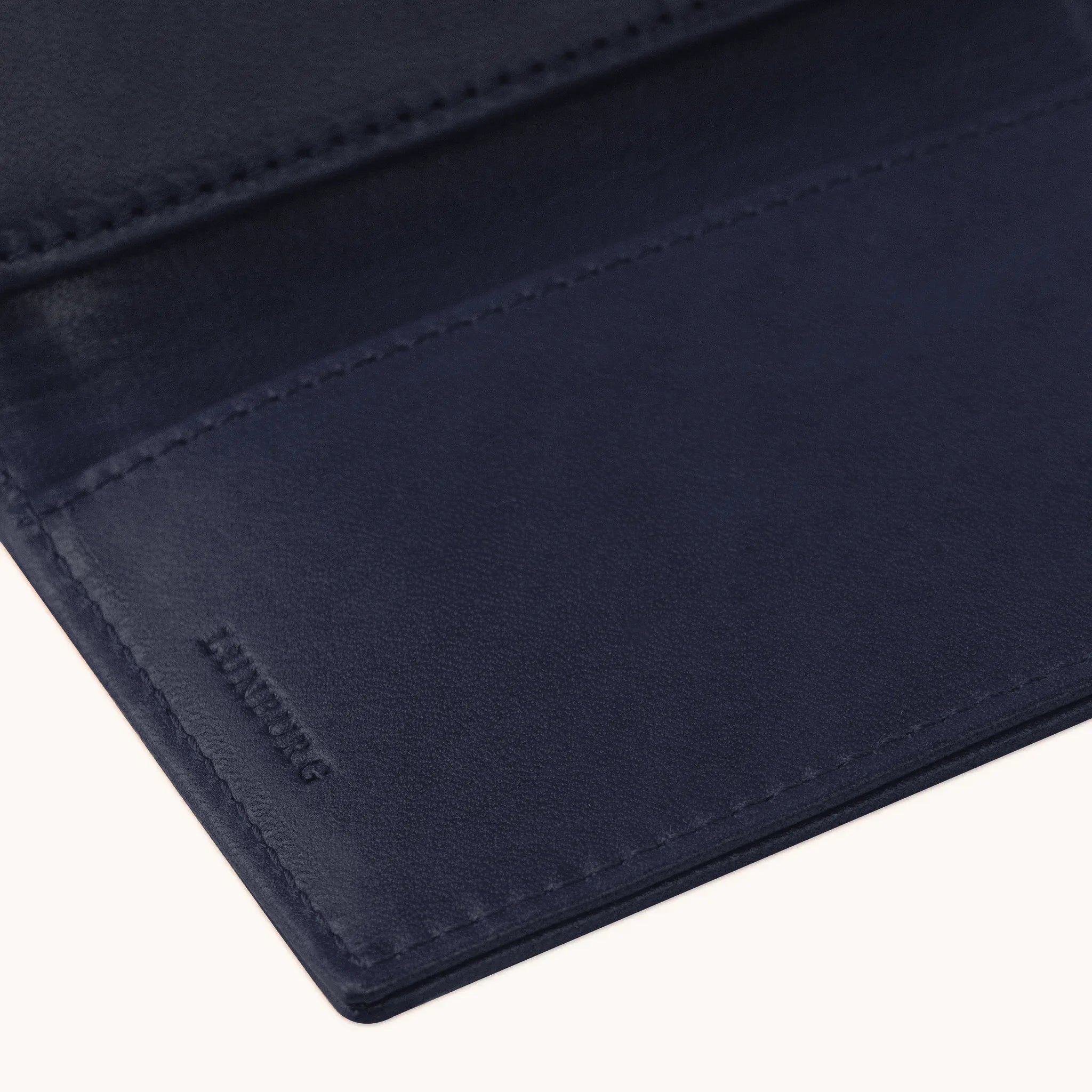 Lunburg Signet Passport Folio in Nocturnal Sapphire, detail view of the interior lower panel showing the heat-embossed Lunburg mark beneath card slots, in vegetable-tanned Perpetual Leather (from Tempesti) with folded edge construction throughout.