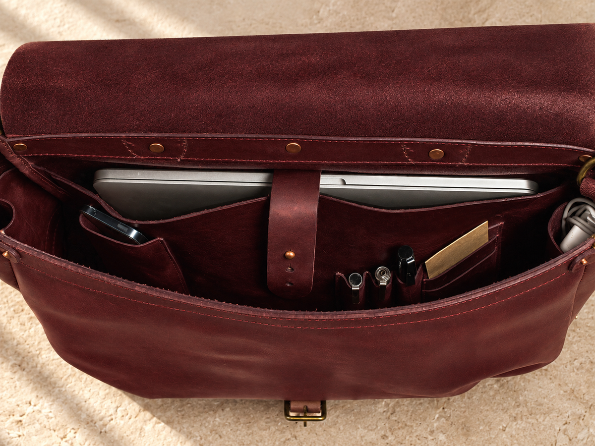 Interior of the illustrative messenger showing a sleeve with a central retention strap, phone pocket, and pen and card openings.