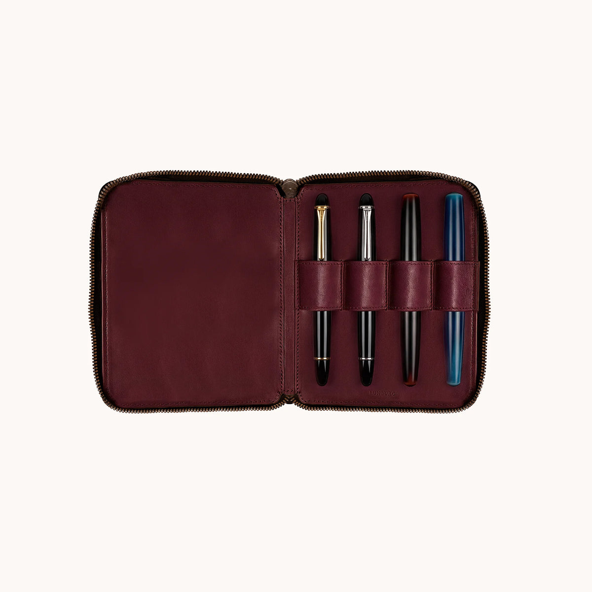 Lunburg Quad Pen Case Curator, interior view with Montblanc Meisterstück with gold trim, Montblanc Meisterstück with platinum trim, Nakaya, and Nakaya blue marbled fountain pen seated in the four leather pen loops, goat leather lining shown across the full interior, heat-embossed Lunburg mark at lower edge, YKK Excella zipper framing the perimeter.