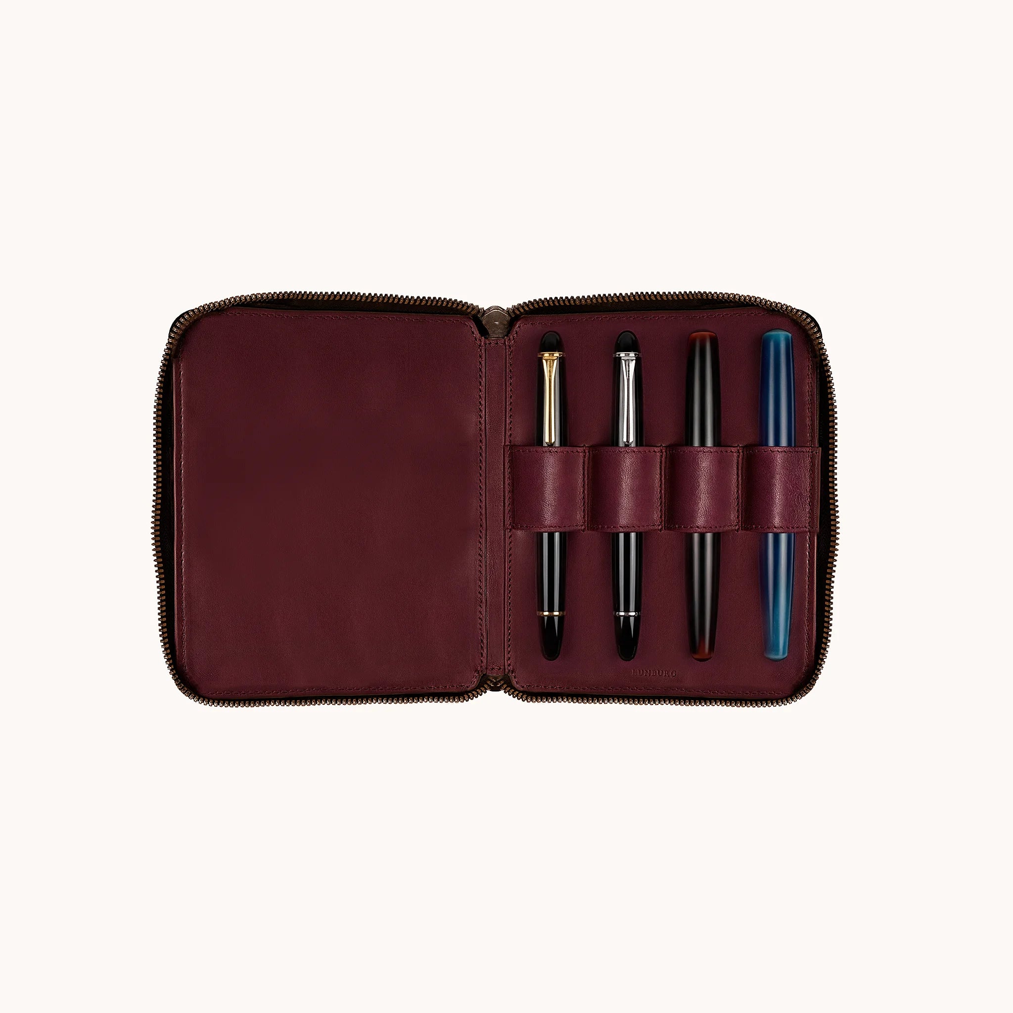 Lunburg Quad Pen Case Curator, interior view with Montblanc Meisterstück with gold trim, Montblanc Meisterstück with platinum trim, Nakaya, and Nakaya blue marbled fountain pen seated in the four leather pen loops, goat leather lining shown across the full interior, heat-embossed Lunburg mark at lower edge, YKK Excella zipper framing the perimeter.