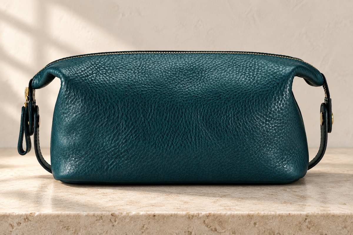 Illustrative low, wide wash bag with a pebble-textured exterior, long top zip, downturned ends and side loops.