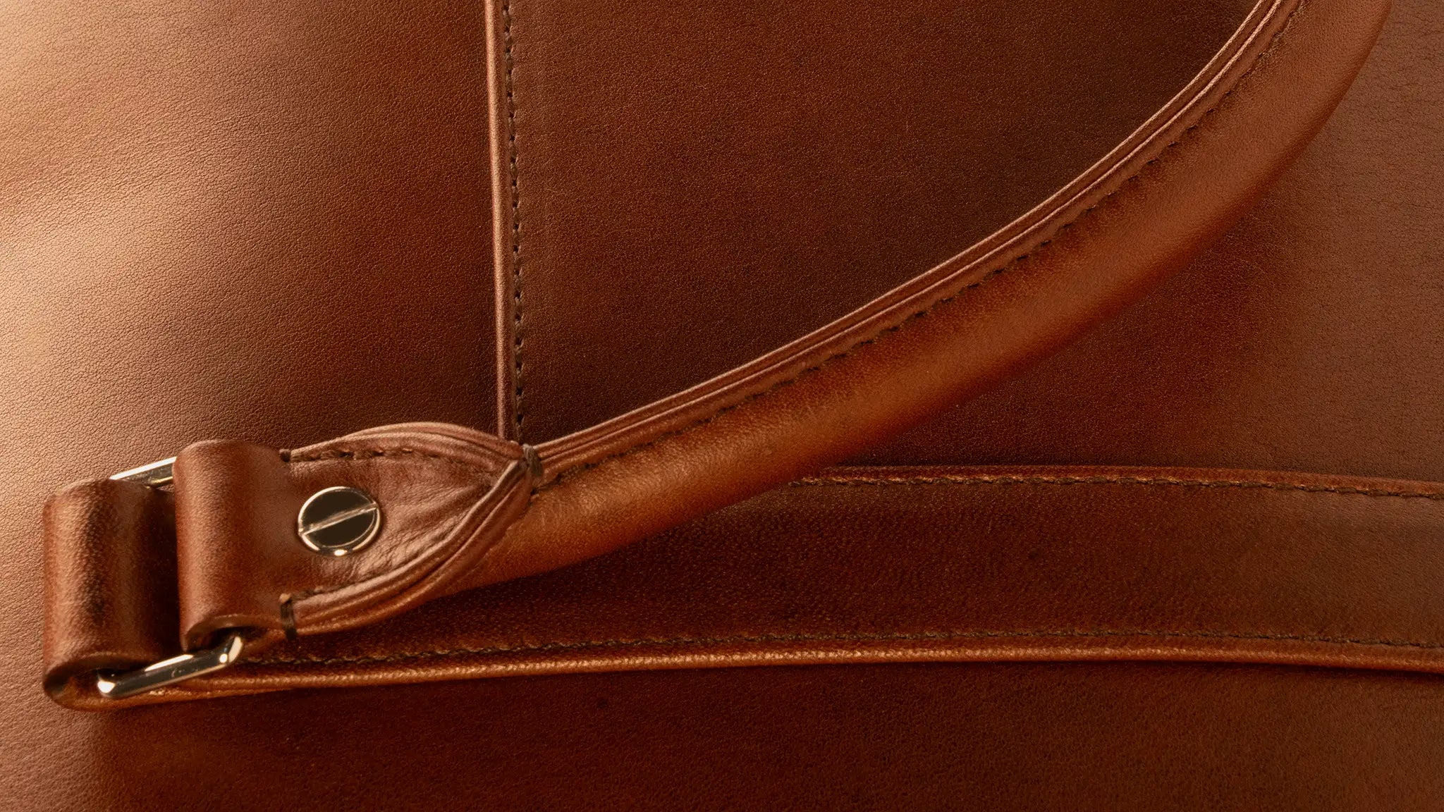Lunburg Opus Briefcase handle detail showing the Rempliage folded edge in Heritage Amber Perpetual Leather (from Tempesti), where grain folds seamlessly upon grain with no paint, no transition, only the unbroken warmth of natural leather wrapped around the handle and slip pocket edges with 316L stainless steel studs. desktop version