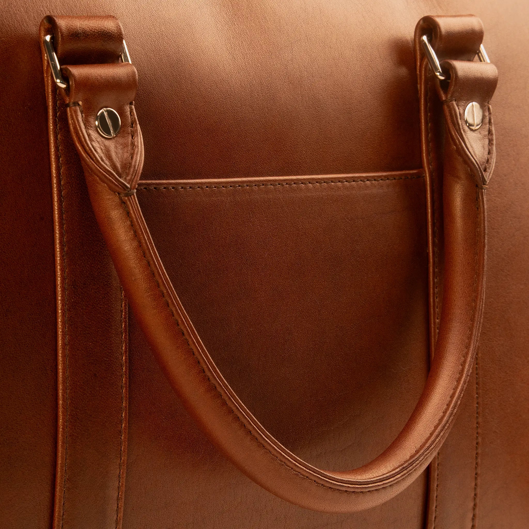 Lunburg Opus Briefcase handle detail showing the Rempliage folded edge in Heritage Amber Perpetual Leather (from Tempesti), where grain folds seamlessly upon grain with no paint, no transition, only the unbroken warmth of natural leather wrapped around the handle and slip pocket edges with 316L stainless steel studs. mobile version