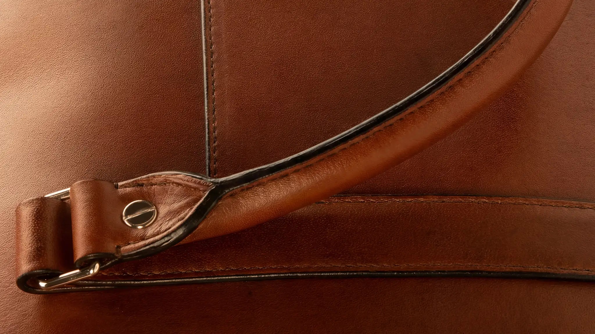 Conventional painted edge construction on a leather briefcase handle for comparison, where the raw cut edge is sealed with black edge paint creating a visible dark line along the handle, straps, and pocket openings, the industry-standard finish that Rempliage's folded edge eliminates entirely. desktop version