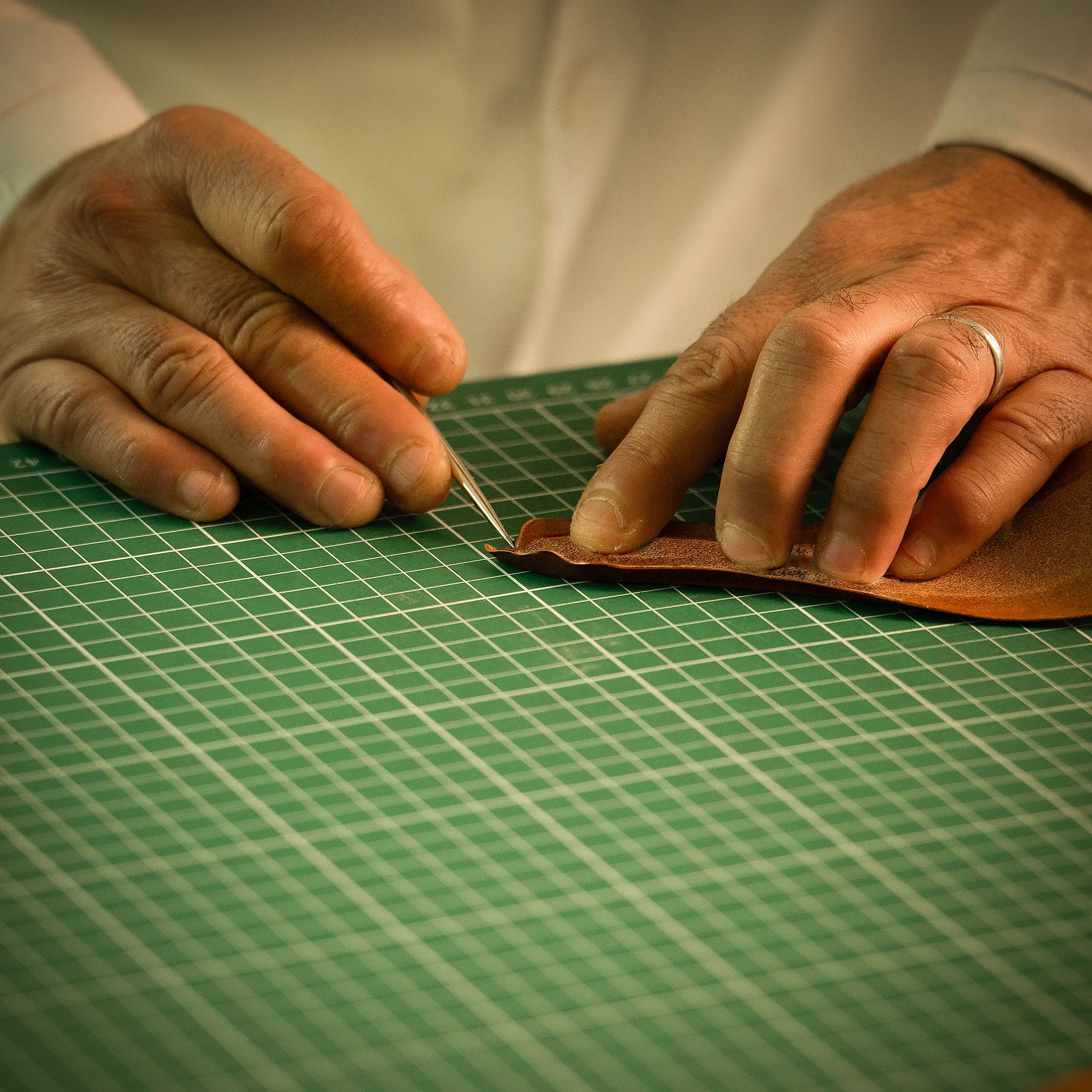 Close-up of artisan's hands at the Lunburg atelier performing high-precision edge folding using an awl on vegetable-tanned Perpetual Leather, the exacting manual technique of Rempliage where tolerances are measured to 0.1 mm.