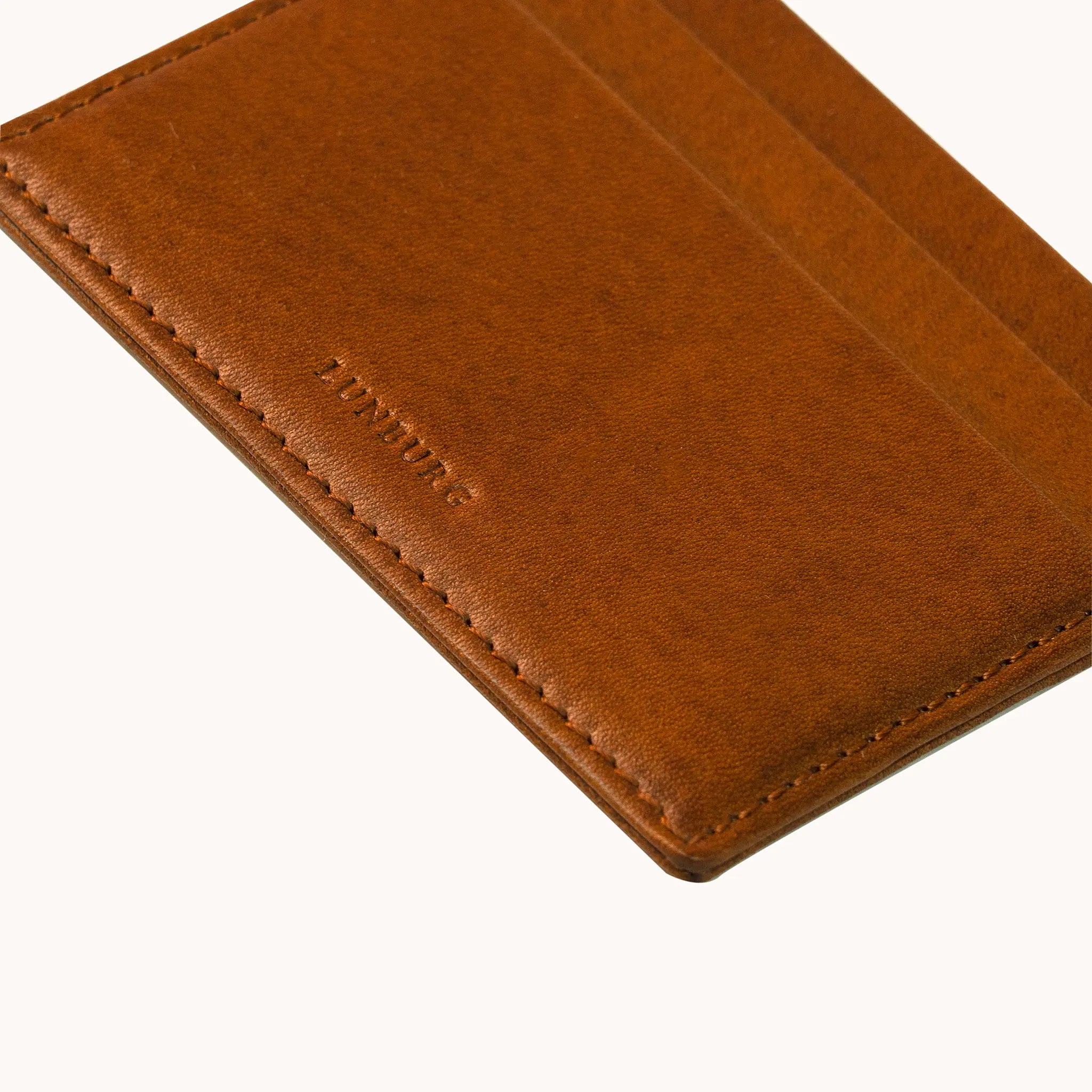 Close-up of the heat-embossed Lunburg mark on the Signet Card Holder in Heritage Amber, with card slot edges, folded edge construction, and saddle stitching visible, in vegetable-tanned Perpetual Leather.