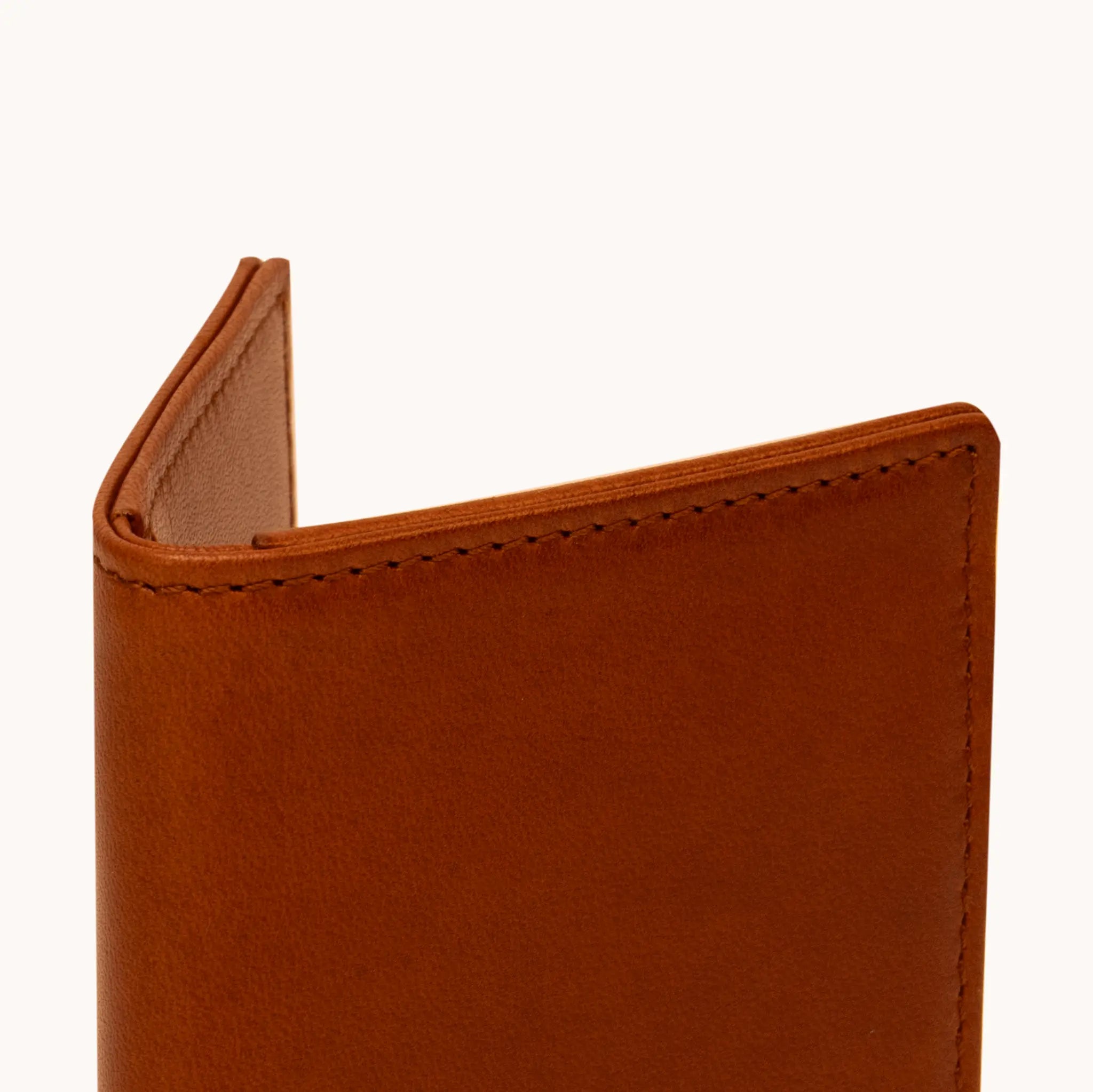 Close-up of the upper spine and fold of the Lunburg Small Vertical Signet Wallet in Heritage Amber, showing folded edge construction, edge stitching, and interior glimpse in vegetable-tanned Perpetual Leather.