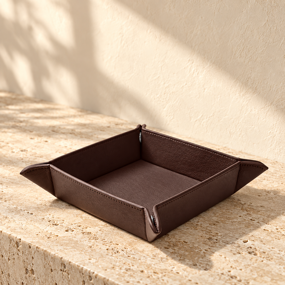 Illustrative snap-corner valet tray, view 1: square open tray with raised sides, pinched projecting corners and perimeter stitching.