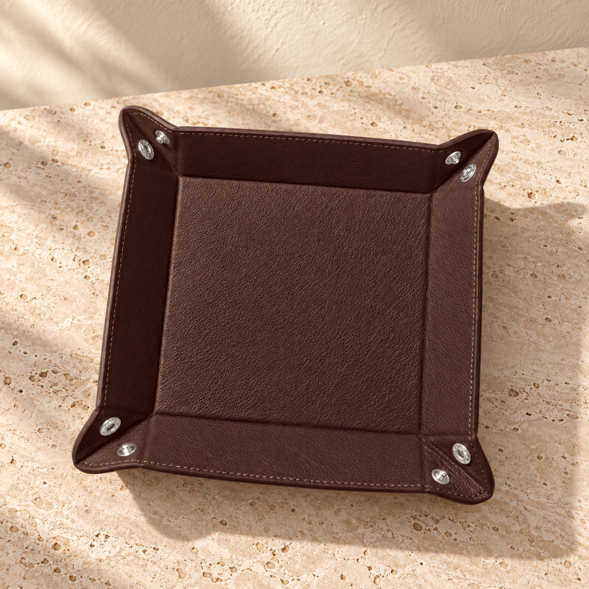 Illustrative snap-corner valet tray, view 3: released corners expose paired metal snap components and stitched perimeter.