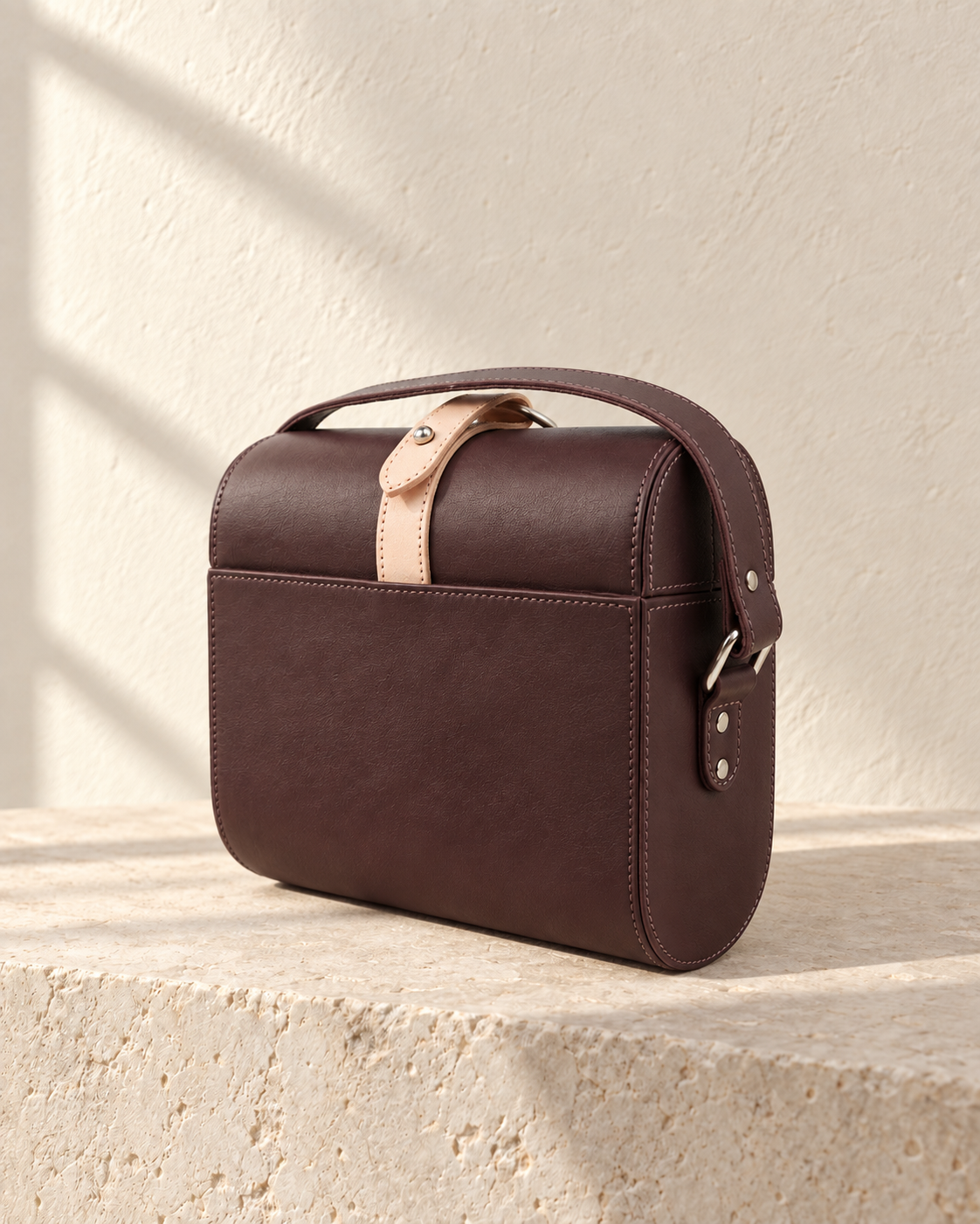 Three-quarter view of the illustrative box crossbody showing its rounded end panel and shoulder strap attached through side rings.