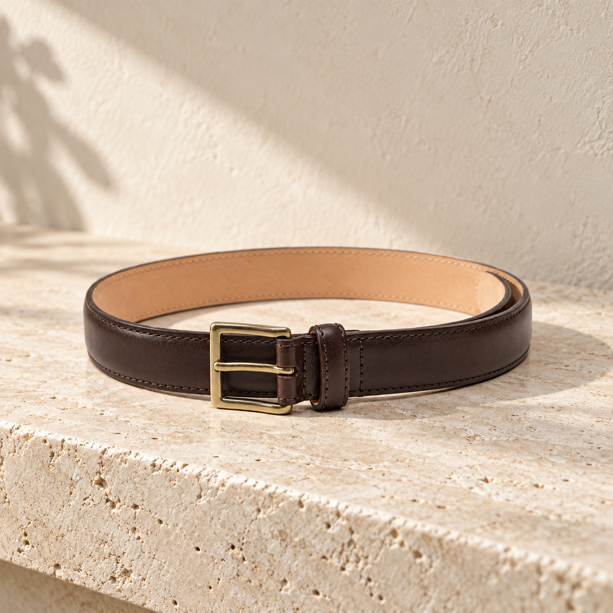 Illustrative stitched tang-buckle belt — coiled dark strap with tan underside, stitch lines along both long edges, rectangular single-prong buckle and keeper.