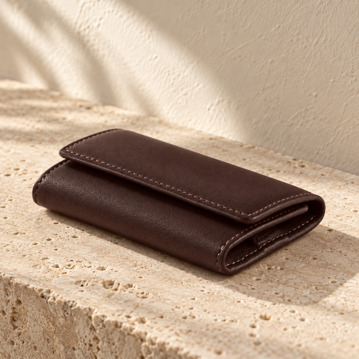 Illustrative trifold hook key case shown closed, with a narrow overlapping flap and visible border stitching.
