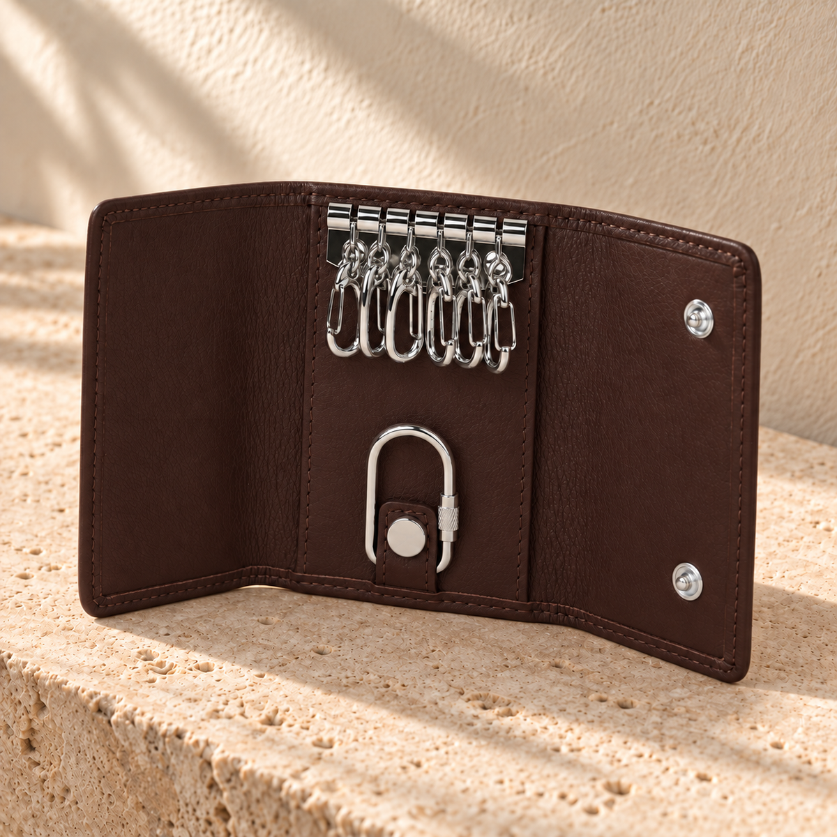 Open illustrative trifold key case with six upper hooks, two snap sockets on the right flap and a lower ring held by a snap tab.