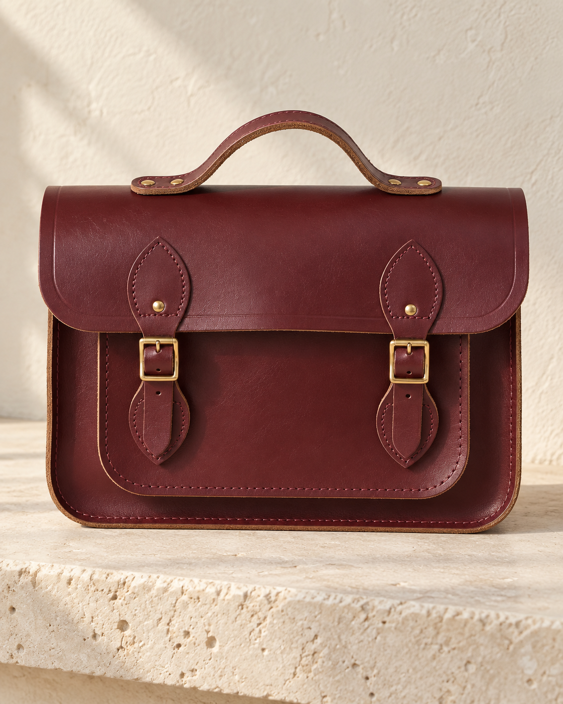 Illustrative satchel handbag with a broad flap, twin buckle straps, leaf-shaped mounts and a short bridge handle.