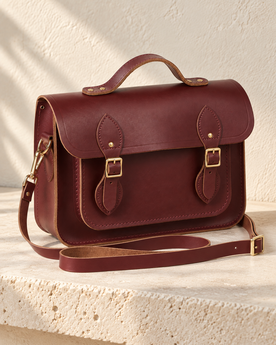 Three-quarter view of the illustrative satchel showing an applied front pocket, detachable shoulder strap and contrasting cut edges.