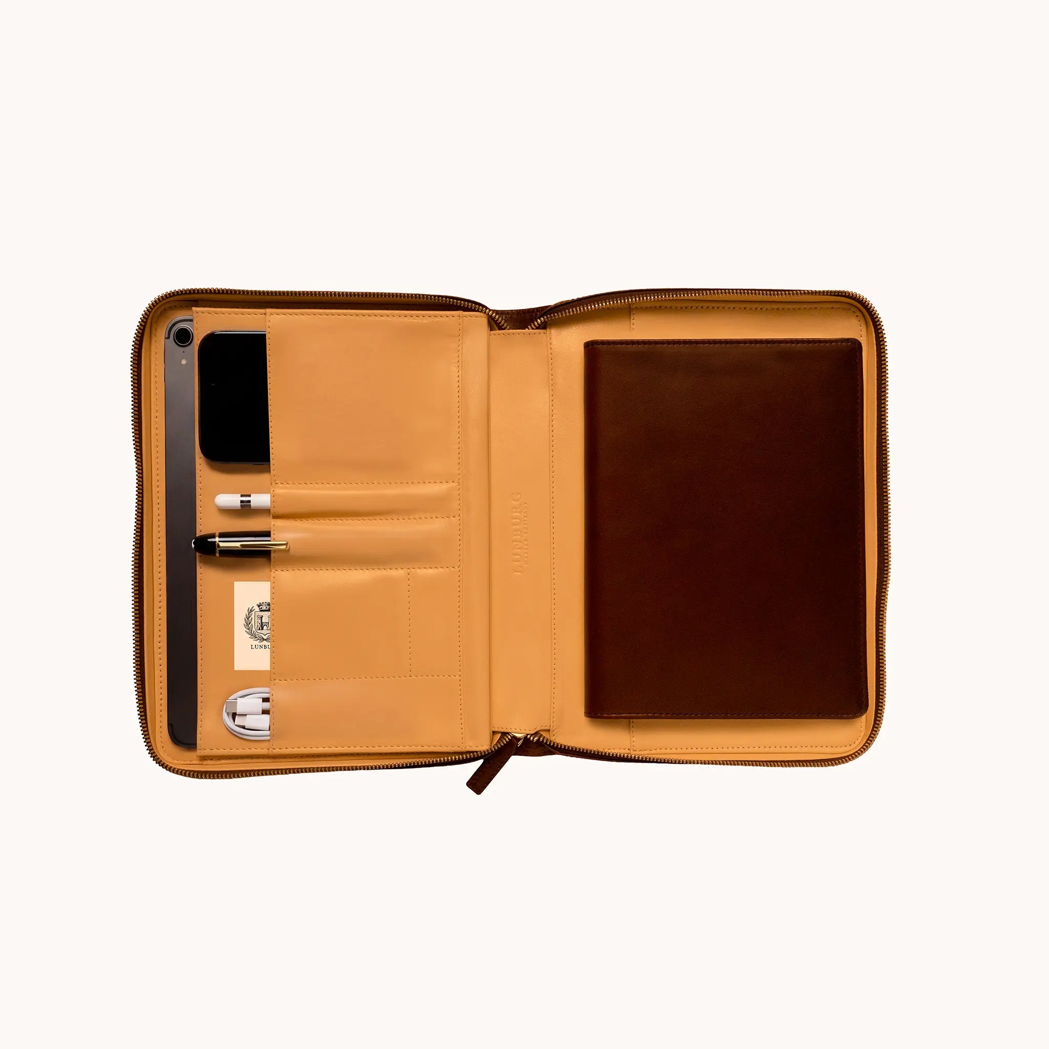 Lunburg Memoir Workstation in Burnt Timber, open interior view styled with a tablet, pen, cable, and Lunburg Memoir Notebook Cover, demonstrating the goat leather lining compartments and organisational layout, in vegetable-tanned Perpetual Leather (from Tempesti) with folded edge construction throughout.
