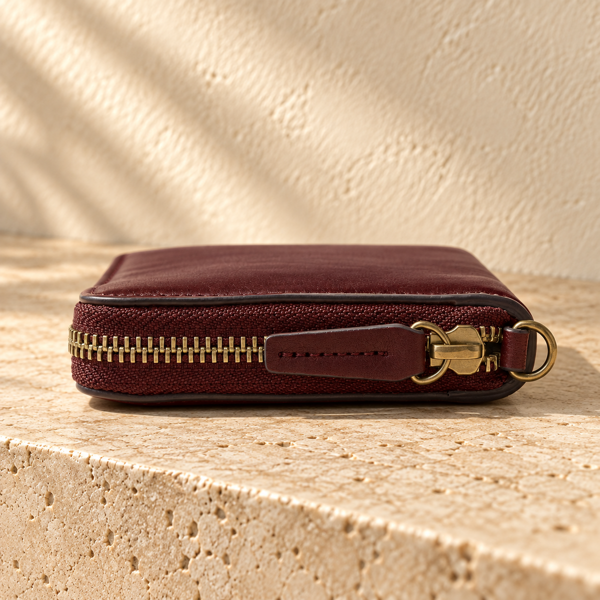 Illustrative zip-around divided wallet — end view shows zip teeth/tape, one outer slider, a separate end D-ring, dark finished edge and stitched pull; no wrist strap is attached.