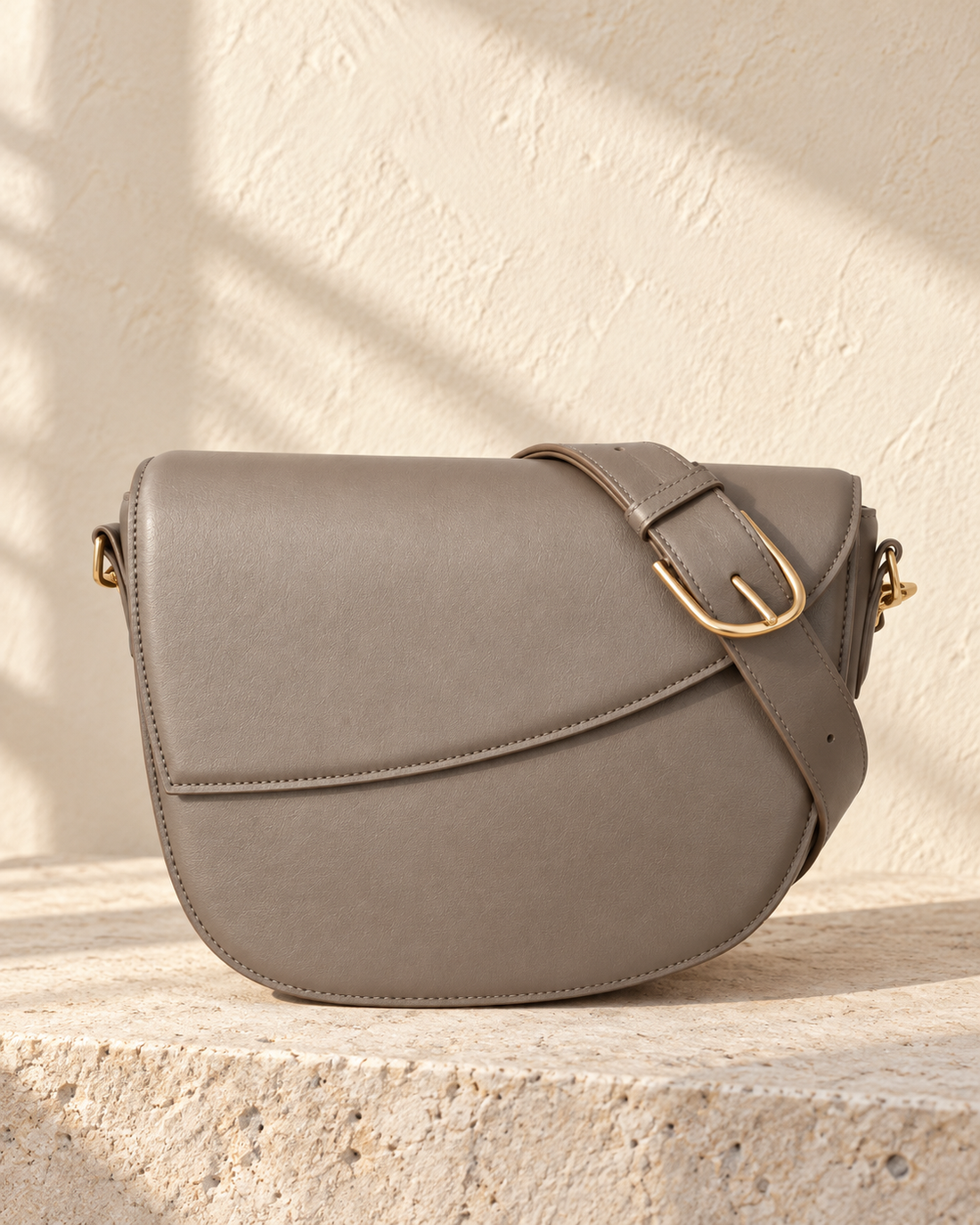 Illustrative rounded crossbody with an asymmetric curved flap and visible stitching around its perimeter.