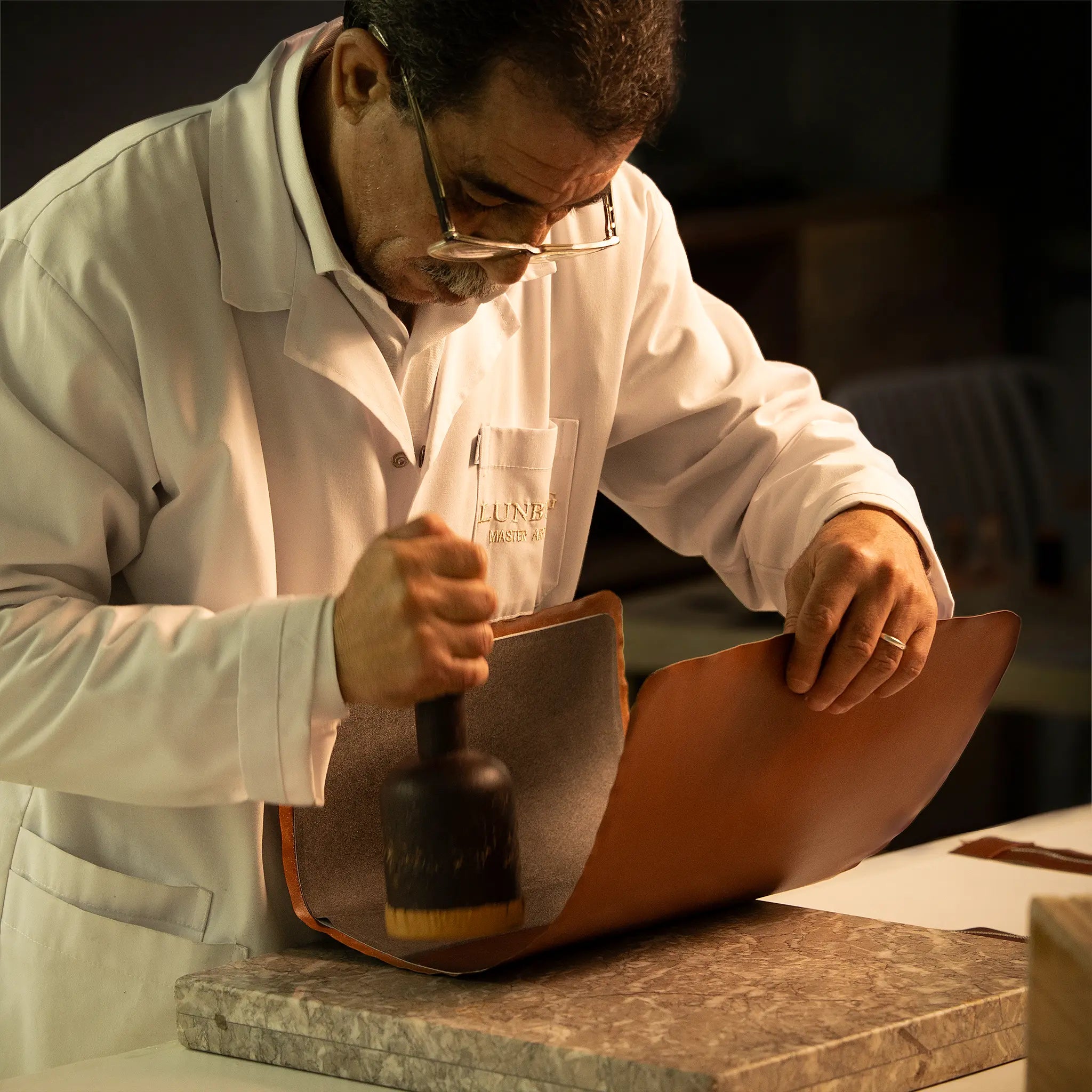 Lunburg Master Artisan setting a folded edge with a rempliage hammer on a marble slab at the Fes atelier, the concentrated focus of a craftsman whose mastery the Lunburg Artisan Fund exists to preserve and transmit.