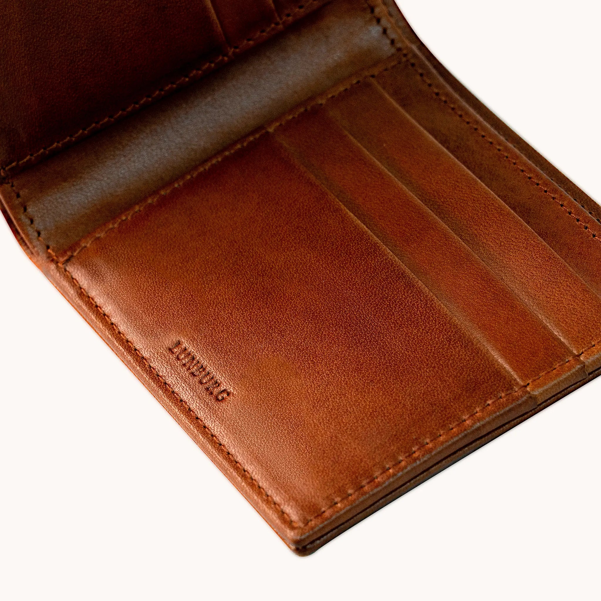 Close-up angled view of the Lunburg Horizontal Signet Bifold Wallet interior in Heritage Amber, showing card slots, heat-embossed Lunburg mark, folded edge construction, and leather grain in vegetable-tanned Perpetual Leather.