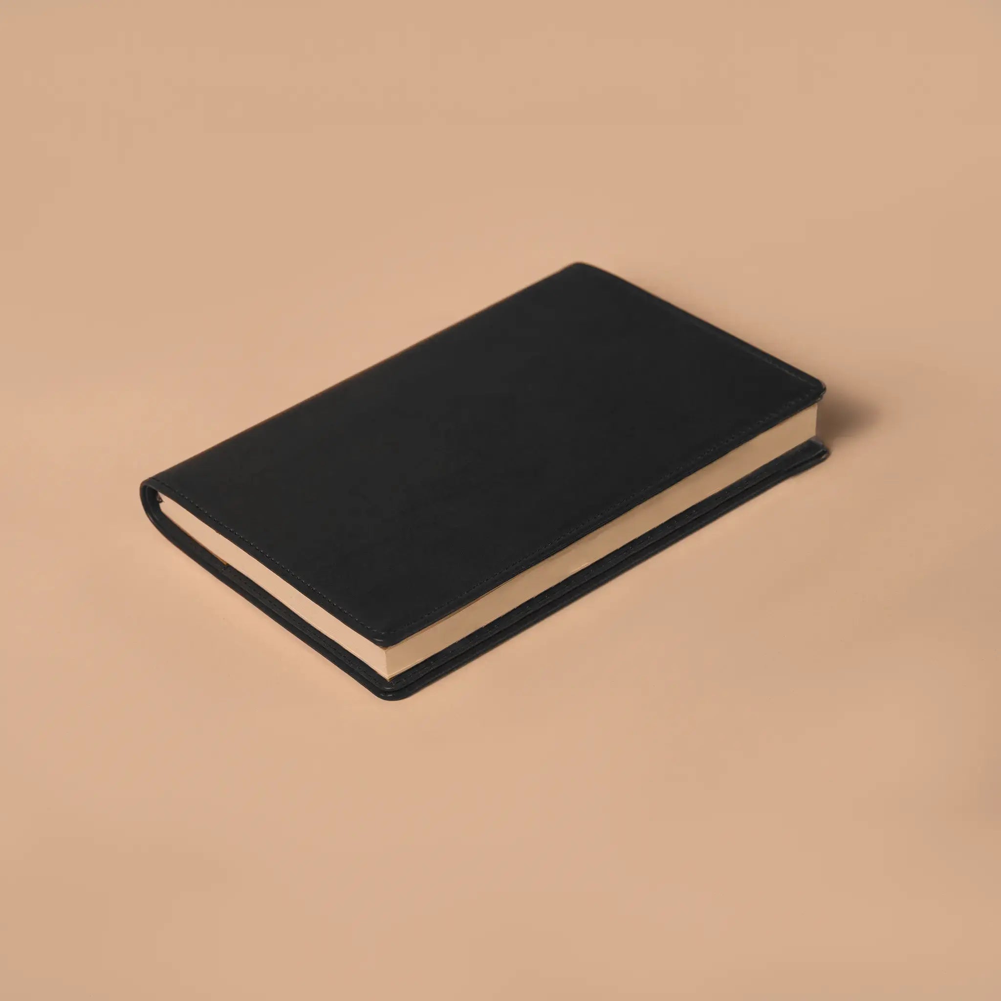 Lunburg Memoir Notebook Cover in Burnt Timber with an A5 notebook inserted, resting on a table at a three-quarter angle showing the leather cover's profile, spine, and page block, in vegetable-tanned Perpetual Leather (from Tempesti) with folded edge construction.