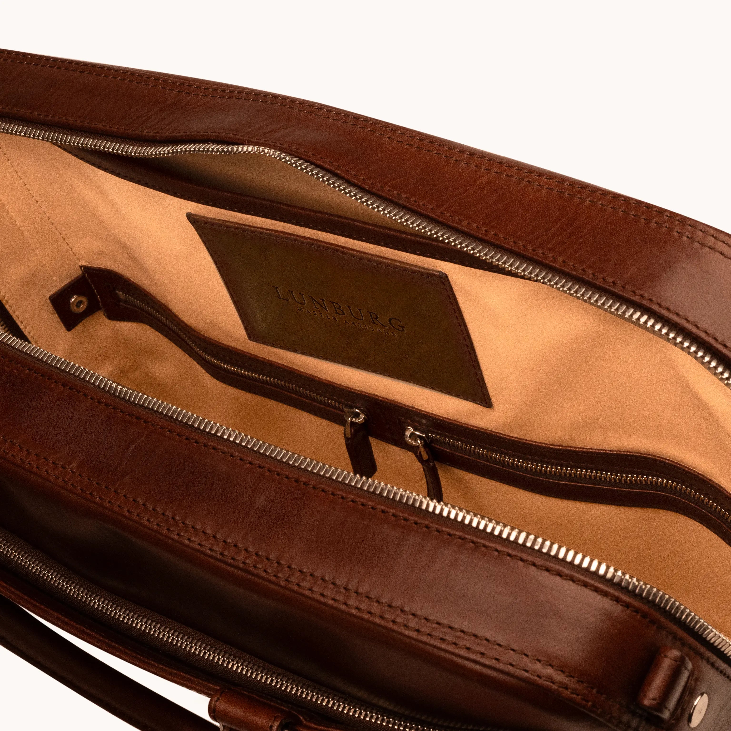 Lunburg Opus Briefcase in Deep Mahogany opened to reveal the document compartment with goat leather lining, interior Lunburg label, zippered pocket, and 316L stainless steel hardware, in vegetable-tanned Perpetual Leather exterior with folded edge construction.