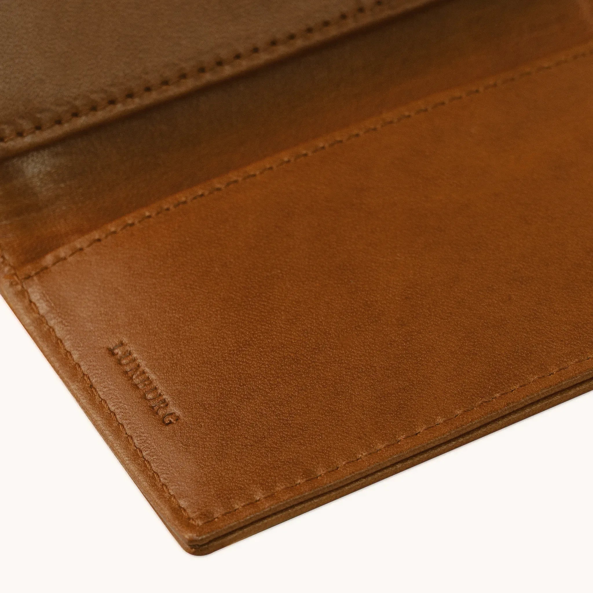 Lunburg Signet Passport Folio in Heritage Amber, detail view of the interior lower panel showing the heat-embossed Lunburg mark beneath card slots, in vegetable-tanned Perpetual Leather (from Tempesti) with folded edge construction throughout.