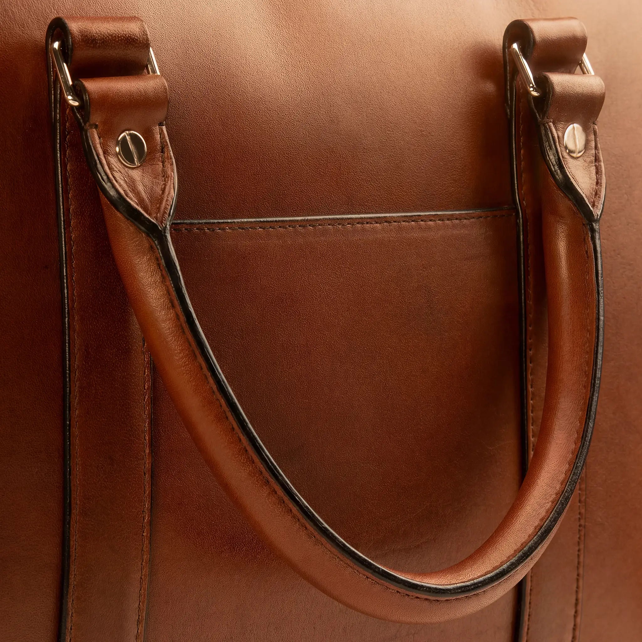 Conventional painted edge construction on a leather briefcase handle for comparison, where the raw cut edge is sealed with black edge paint creating a visible dark line along the handle, straps, and pocket openings, the industry-standard finish that Rempliage's folded edge eliminates entirely. mobile version