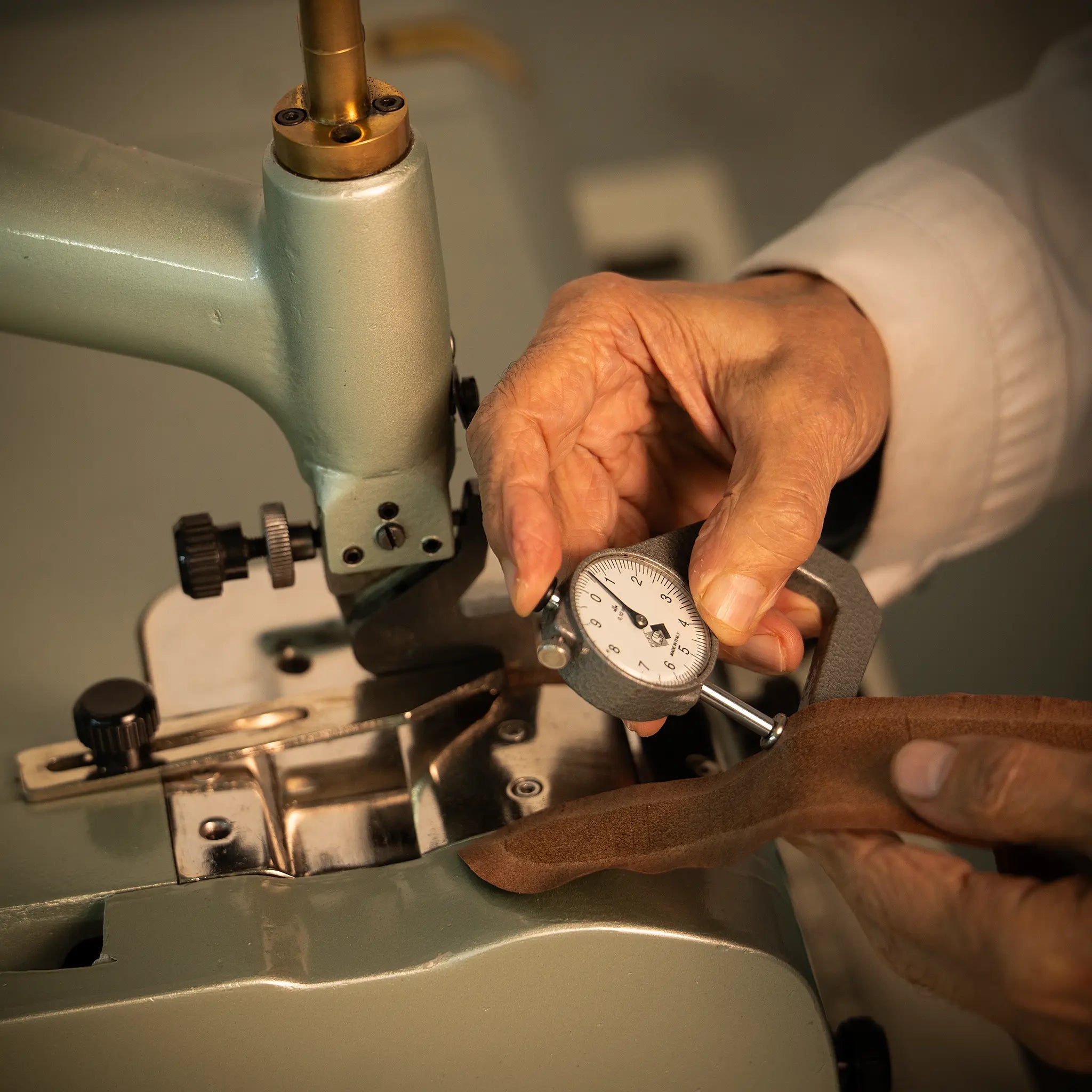 Artisan's hands at the Lunburg atelier measuring leather thickness with a dial gauge at the skiving machine during parage, calibrating to fractions of a millimeter in preparation for the Rempliage folded edge.