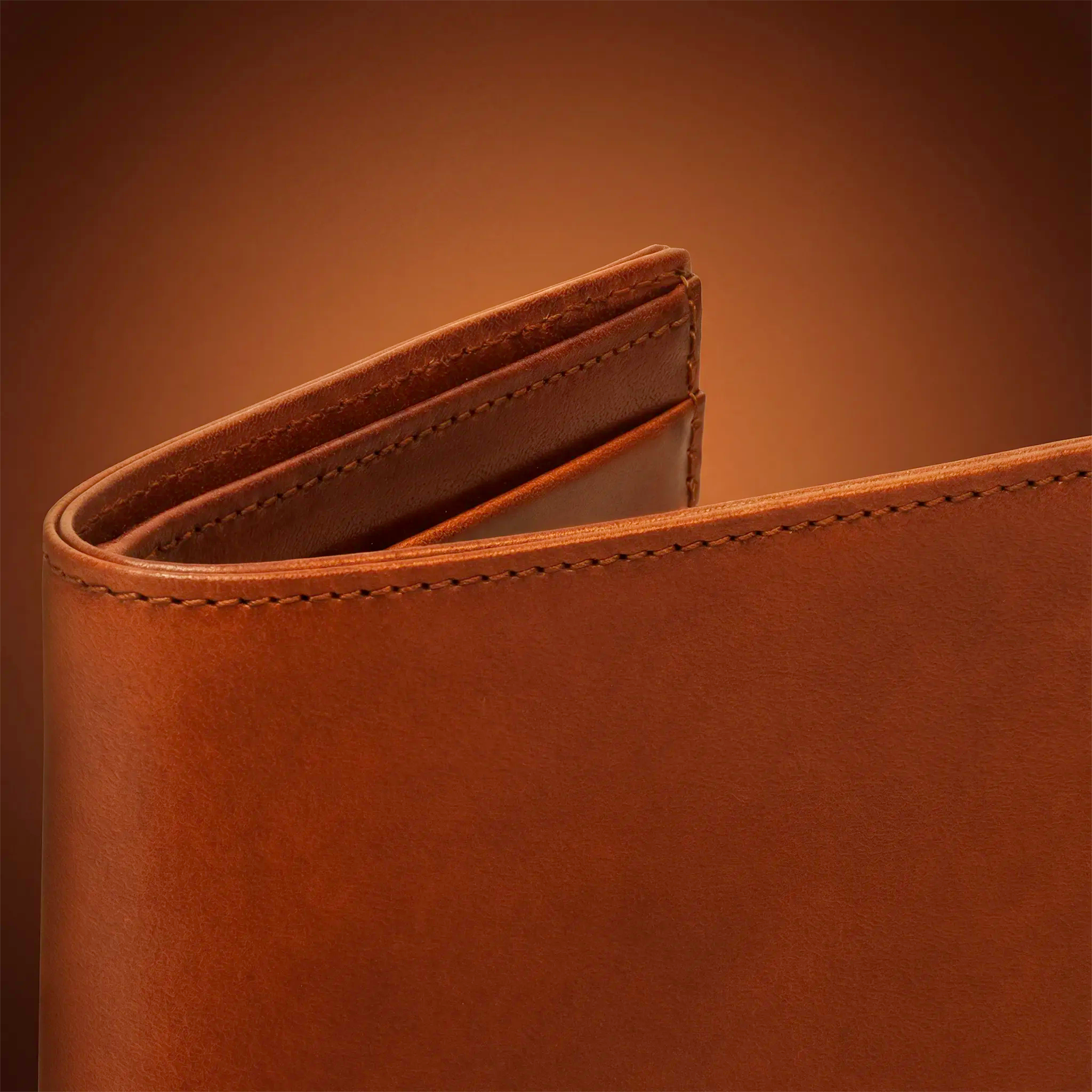 Close-up detail of a Lunburg Signet wallet in Heritage Amber vegetable-tanned Perpetual Leather (from Tempesti), showing the folded edge construction of Rempliage where each edge is reinforced from within and worked until it dissolves into the form — no paint, no exposed seams, only the unbroken warmth of grain.