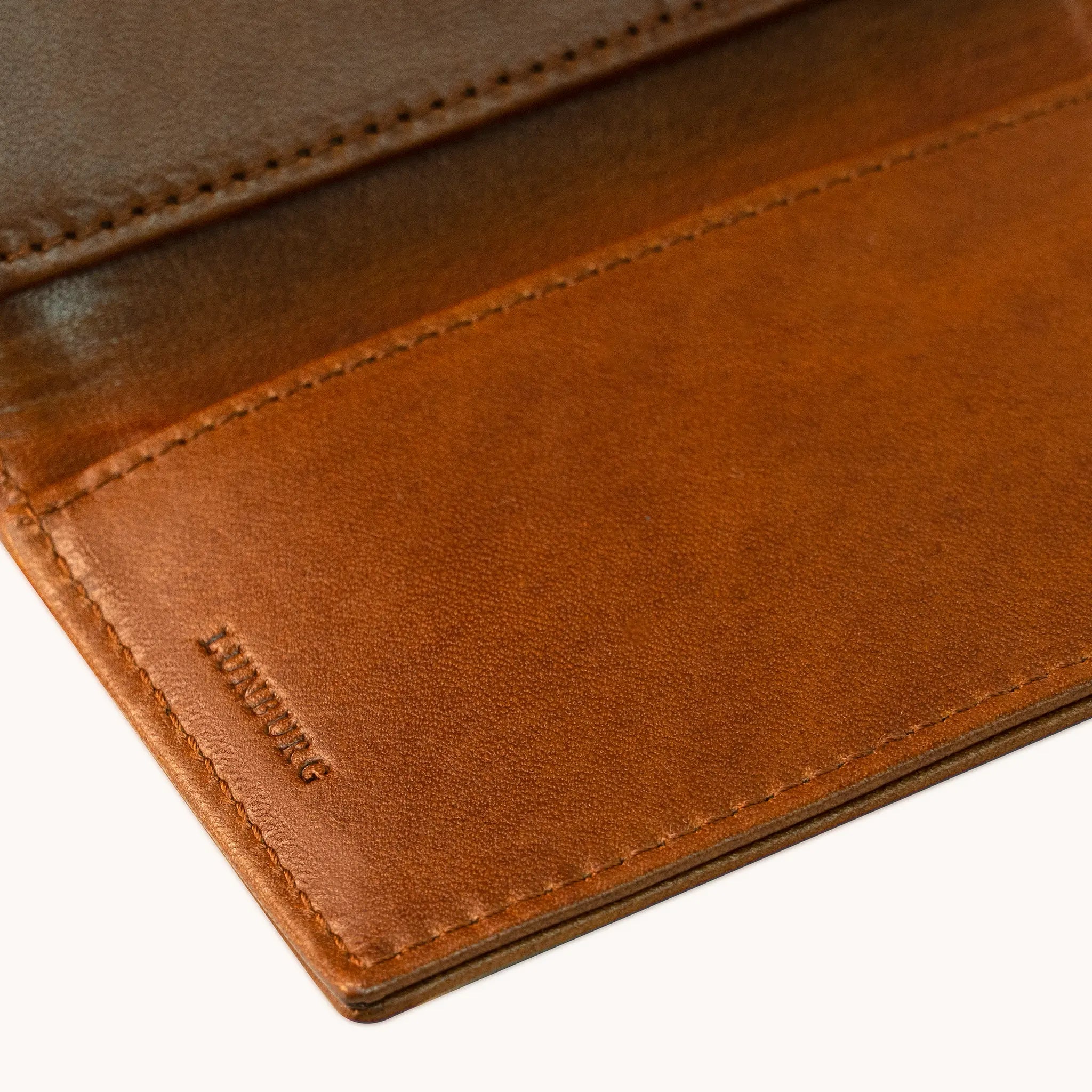 Close-up of the heat-embossed Lunburg mark on the interior of the Small Vertical Signet Wallet in Heritage Amber, with folded edge construction, card slot edge, and saddle stitching visible, in vegetable-tanned Perpetual Leather.