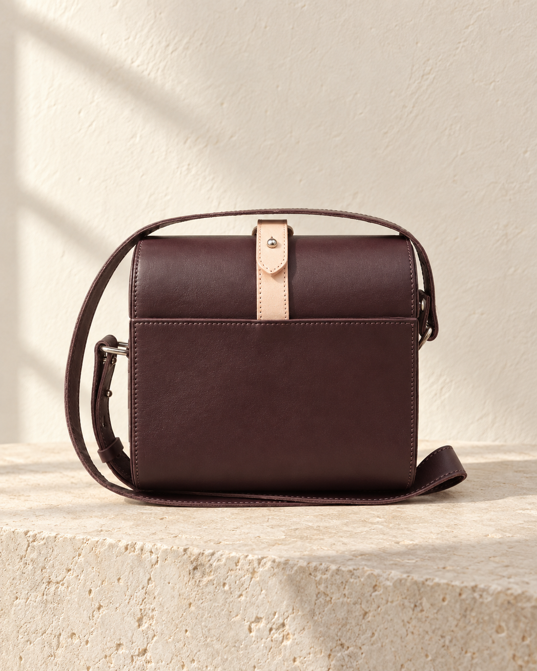 Illustrative box crossbody with rounded ends, stitched end panels and a narrow contrasting strip across the curved top.